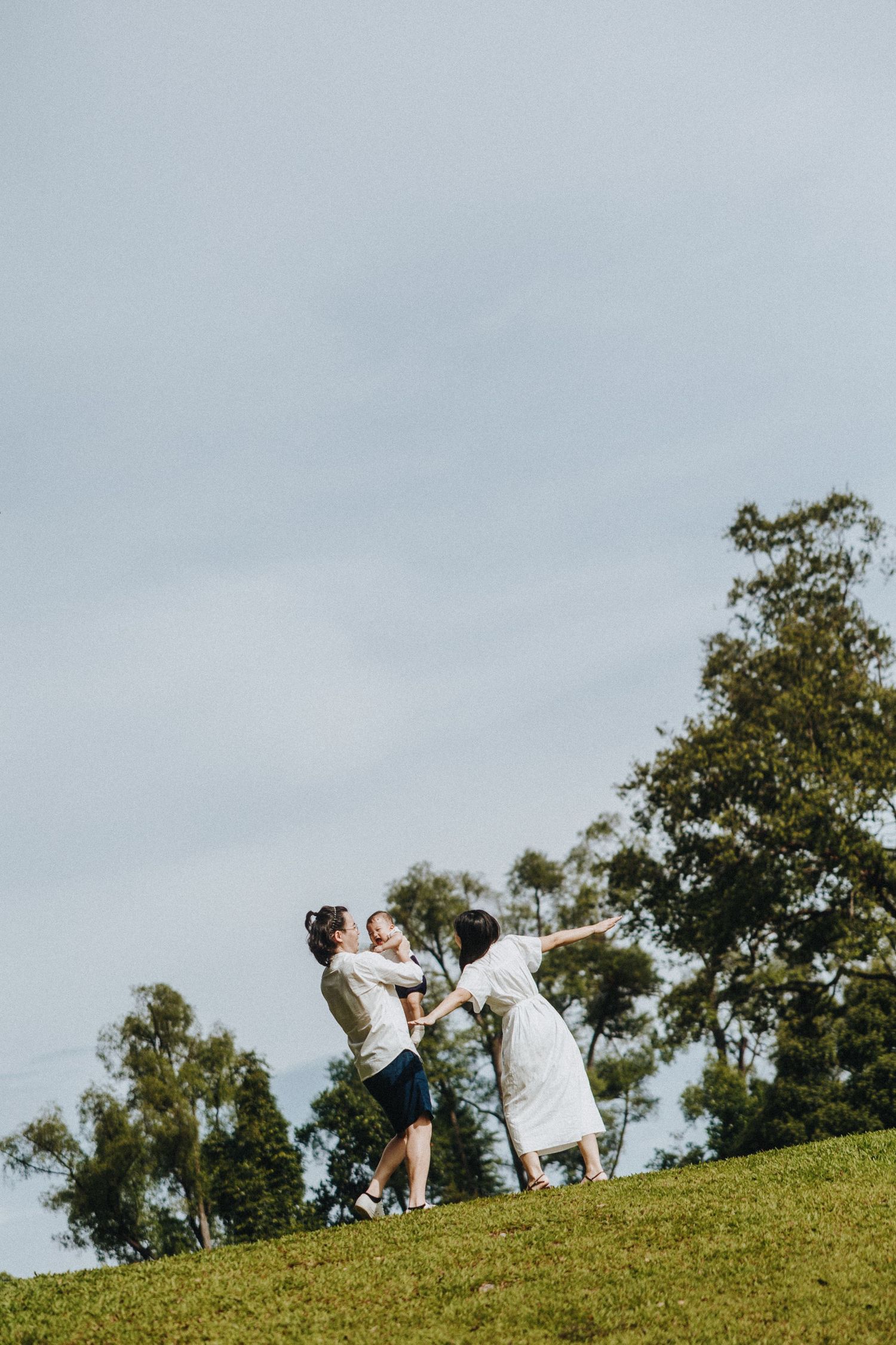 A playful moment captured on a grassy hill against a cloudy sky with trees in the background.