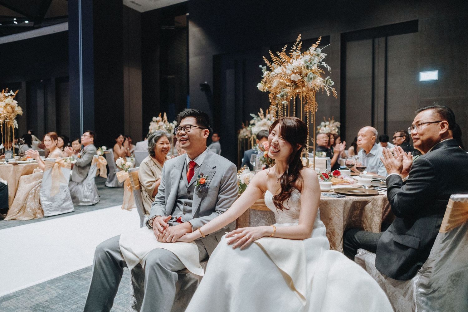 Wedding guests celebrate and clap during an elegant indoor reception with floral decorations and warm lighting.