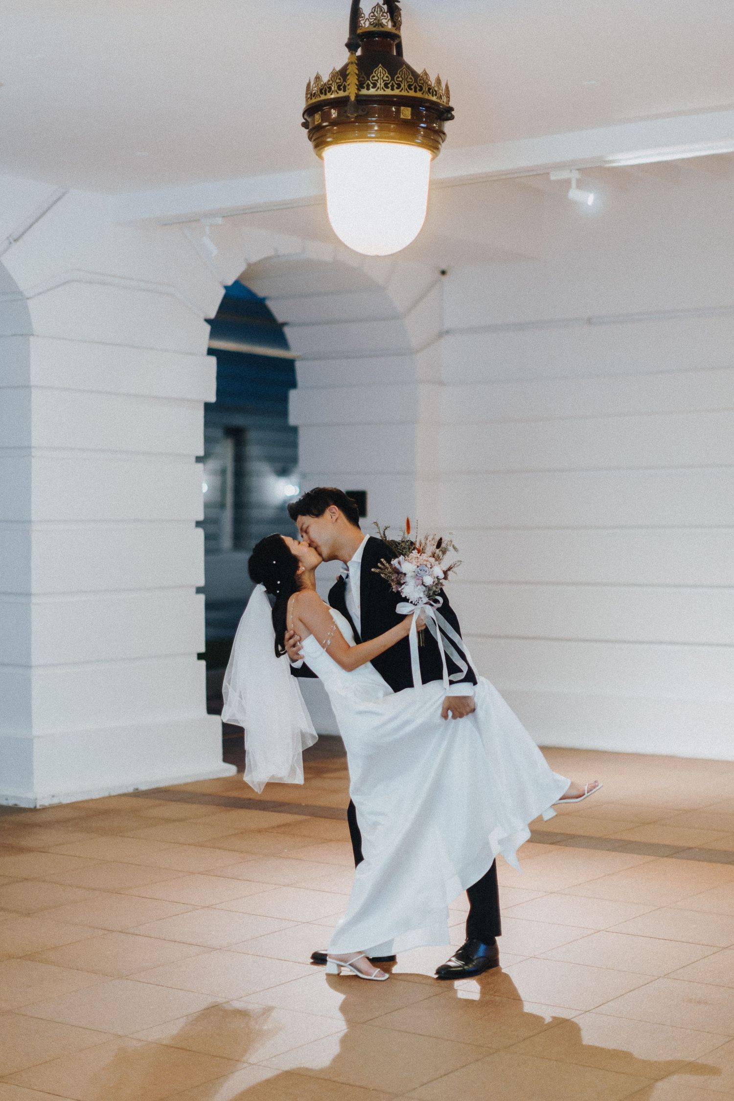 A romantic wedding dance captured under an ornate vintage ceiling light in a white interior.