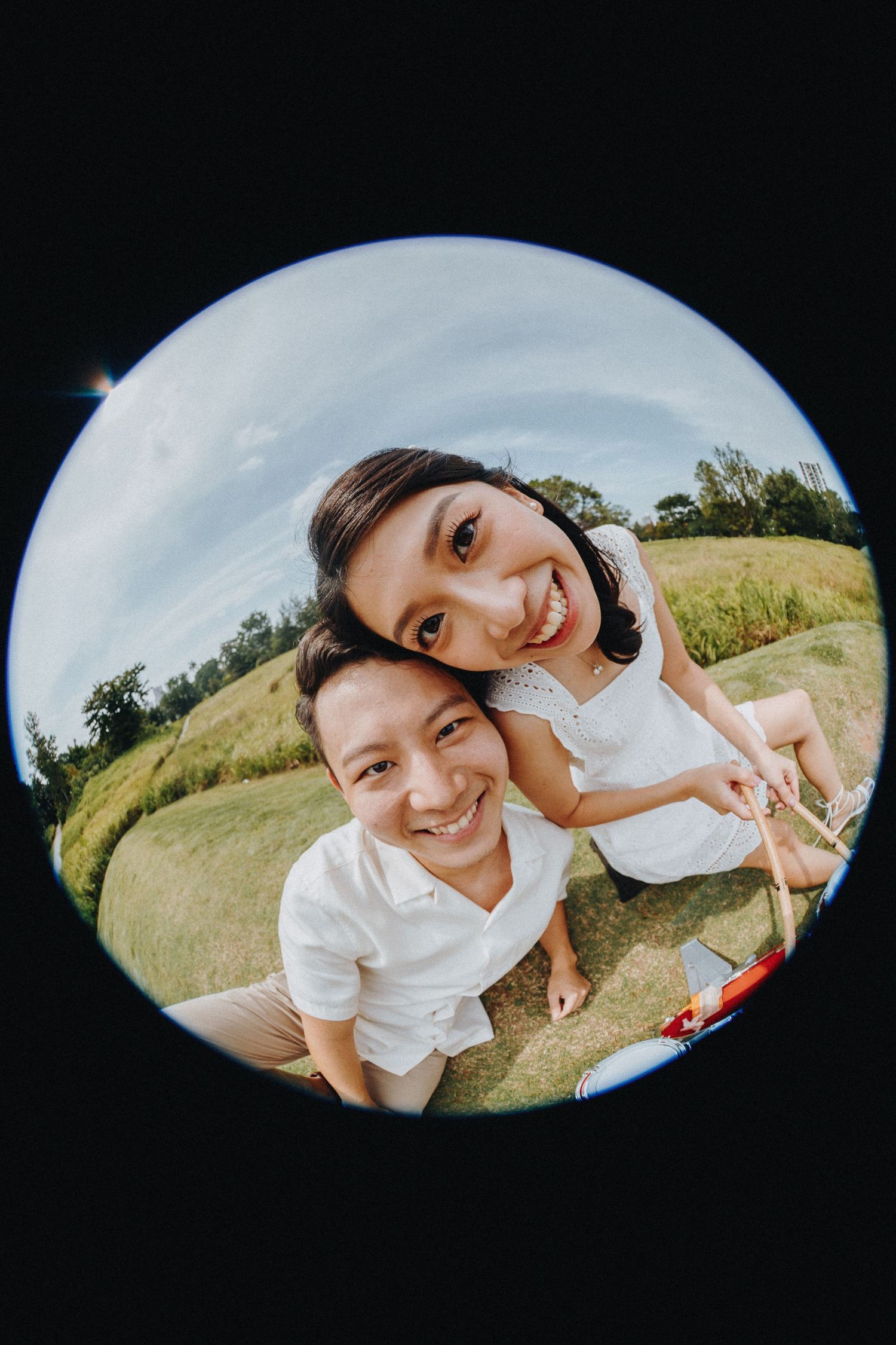 A playful fisheye lens selfie of a couple outdoors on a sunny day.