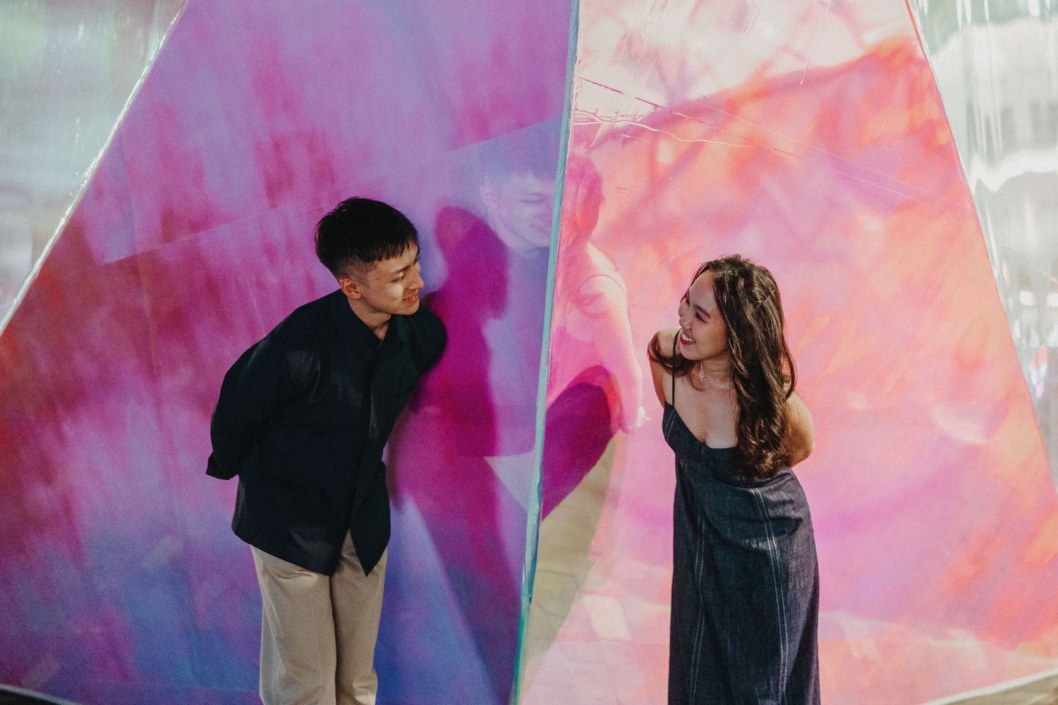 Couple pose against vibrant pink and purple watercolor wall backdrop.