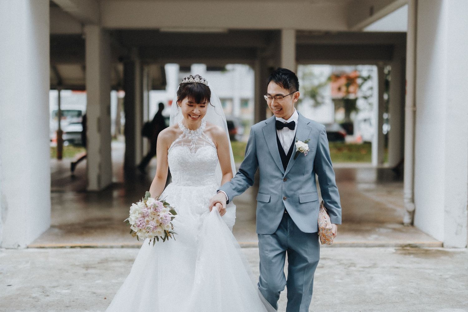 A couple in wedding attire walk together under a covered walkway with white columns.