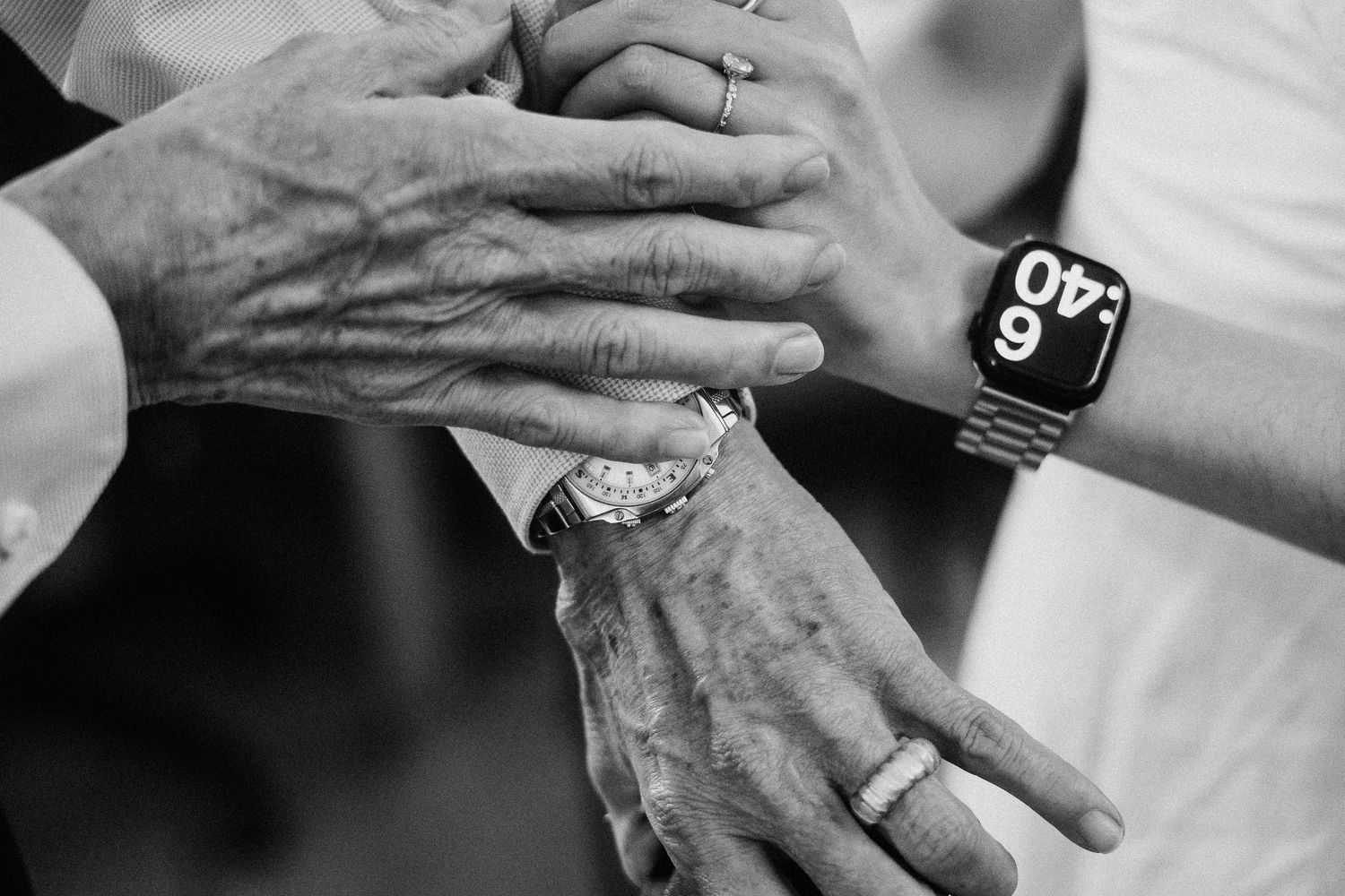 Black and white photo showing hands wearing rings and an Apple Watch, symbolizing a wedding moment or celebration.