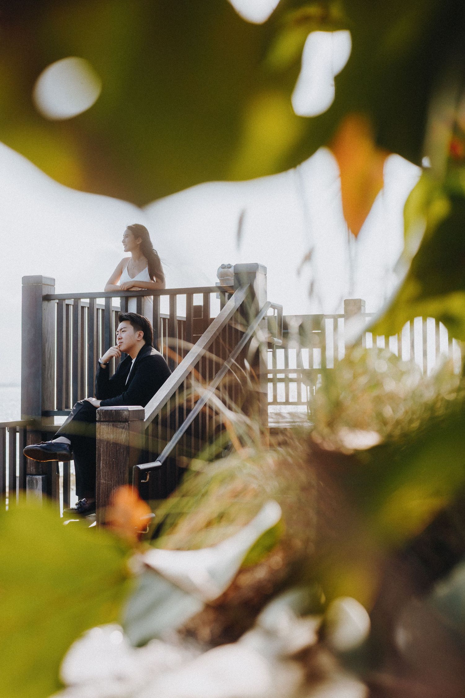 Artistic shot through leaves of people sitting on outdoor deck stairs.