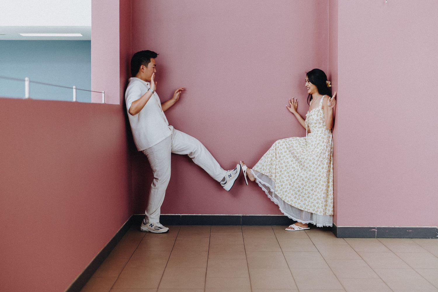 Couple playfully interacts against a pink wall in a modern setting.