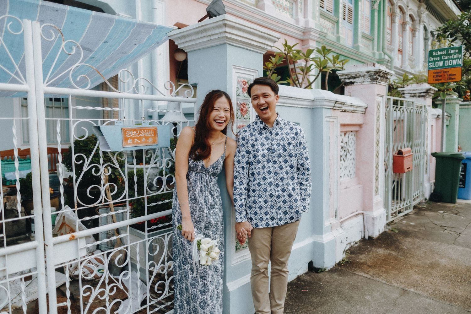 A couple standing in front of a pastel-colored heritage building with ornate white gates.