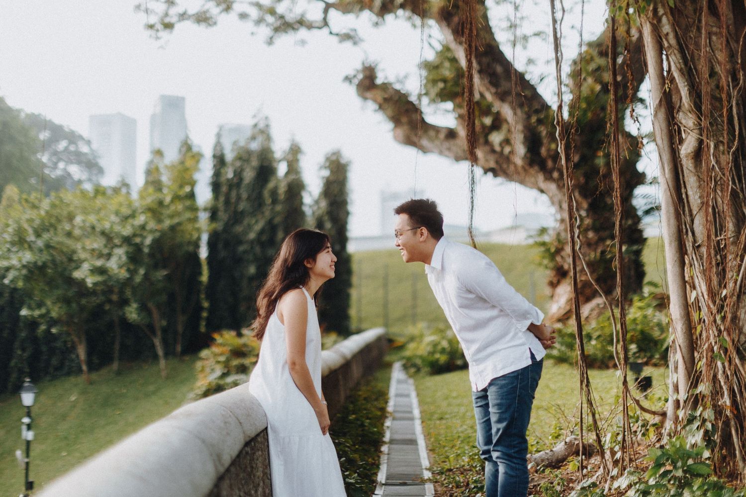 A couple shares a playful moment on a hillside path with cityscape in the background.