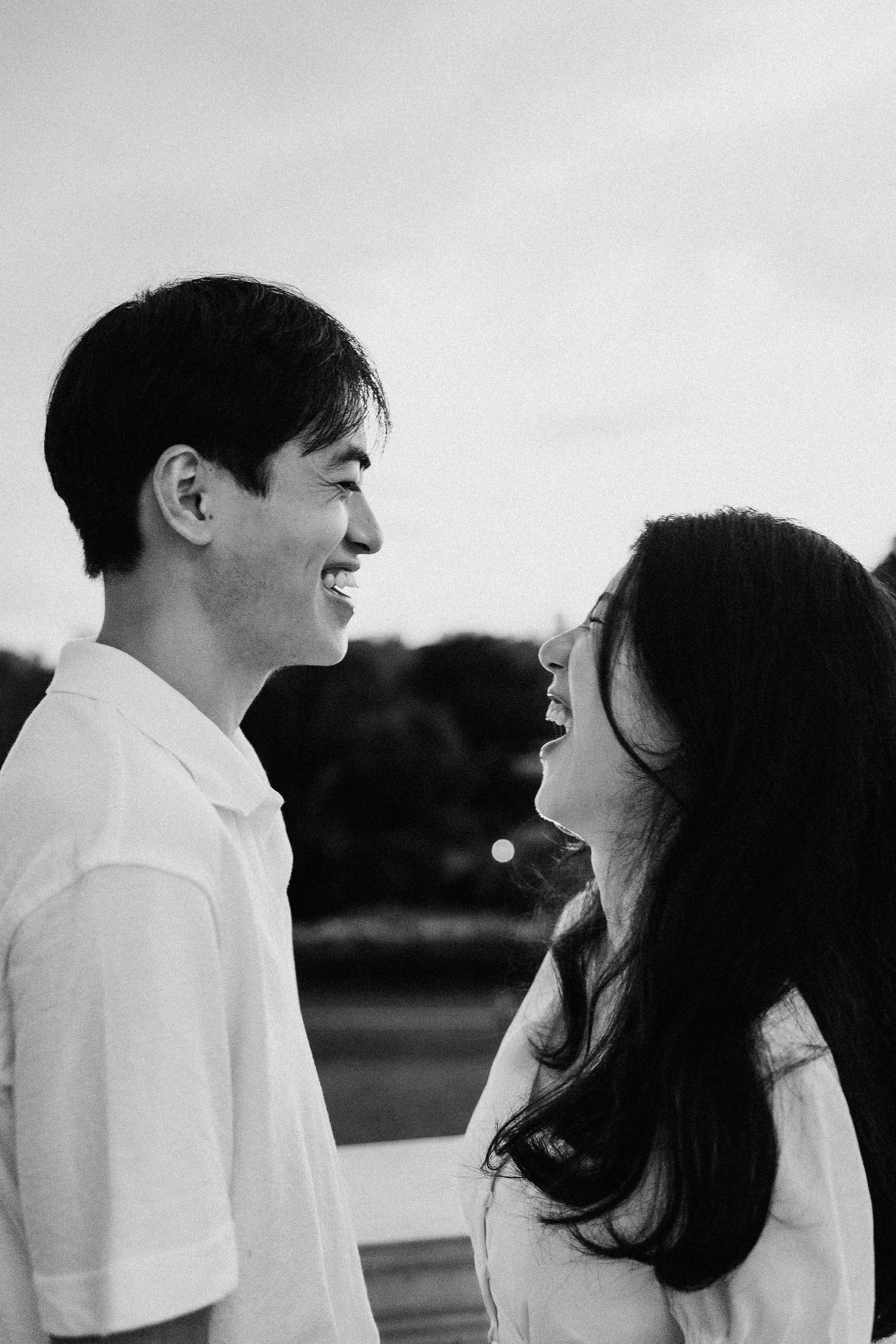 A romantic black and white photo of a couple smiling at each other outdoors.