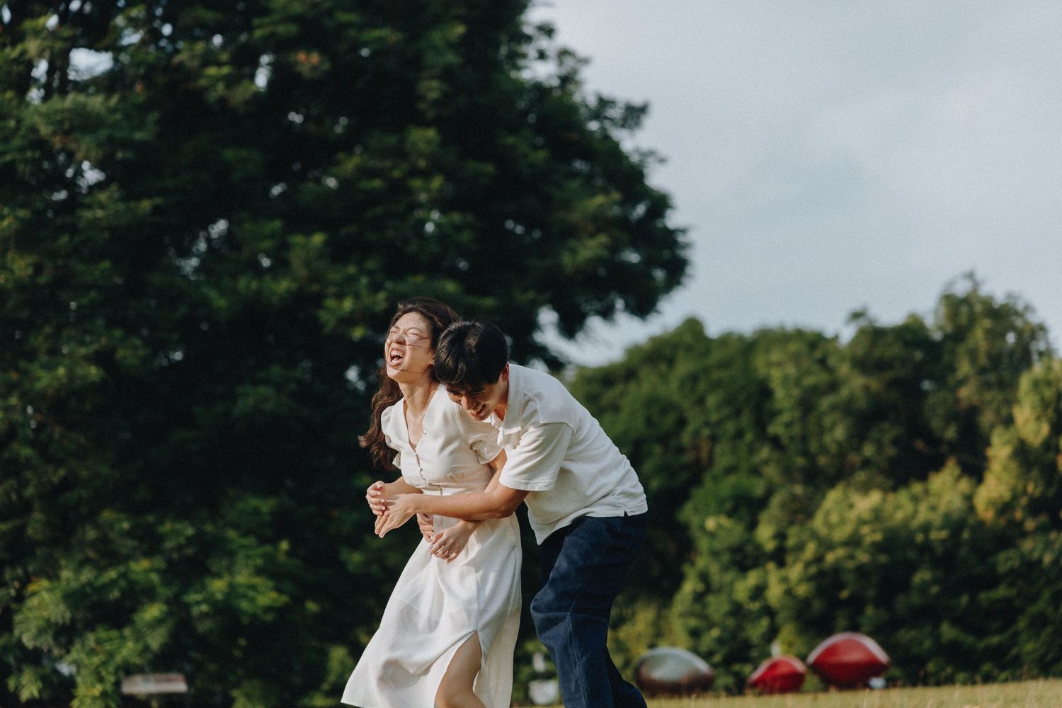A playful moment captured in a green field as a couple shares a joyful embrace.