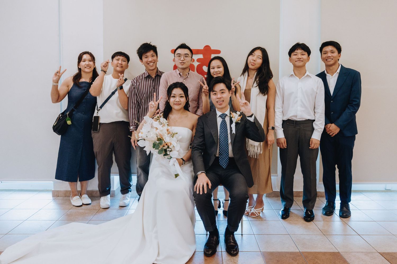 Wedding couple poses with smiling guests in a bright venue, bride holding a bouquet.