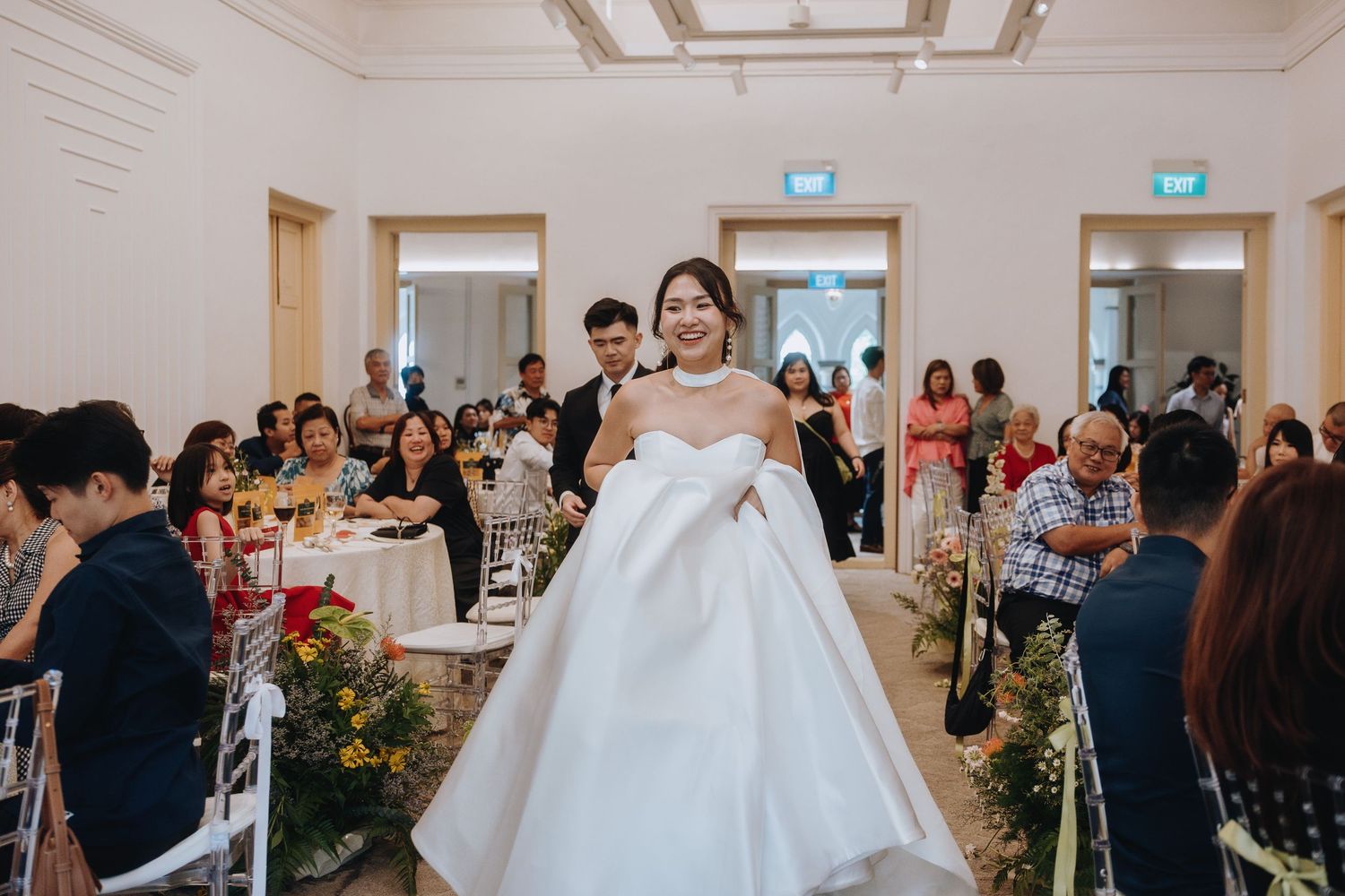 Bride in elegant white ball gown walking through a decorated wedding reception hall filled with guests.