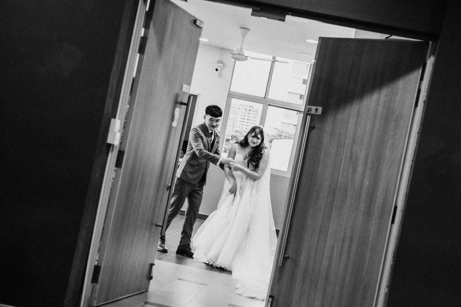 Black and white photo of a couple walking through a doorway in formal wedding attire.