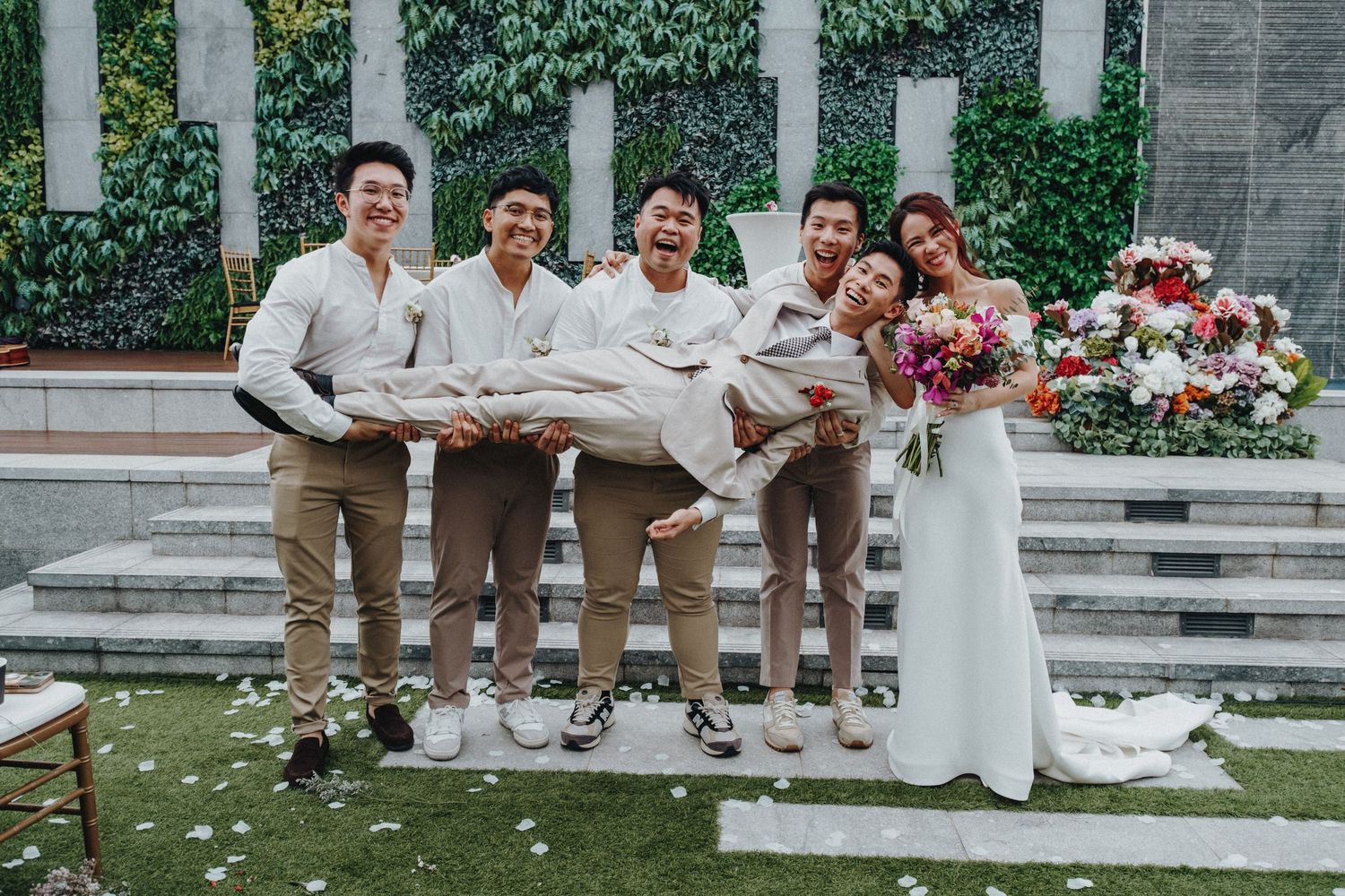 Wedding party poses for a fun group photo on stone steps with a flower-decorated backdrop.