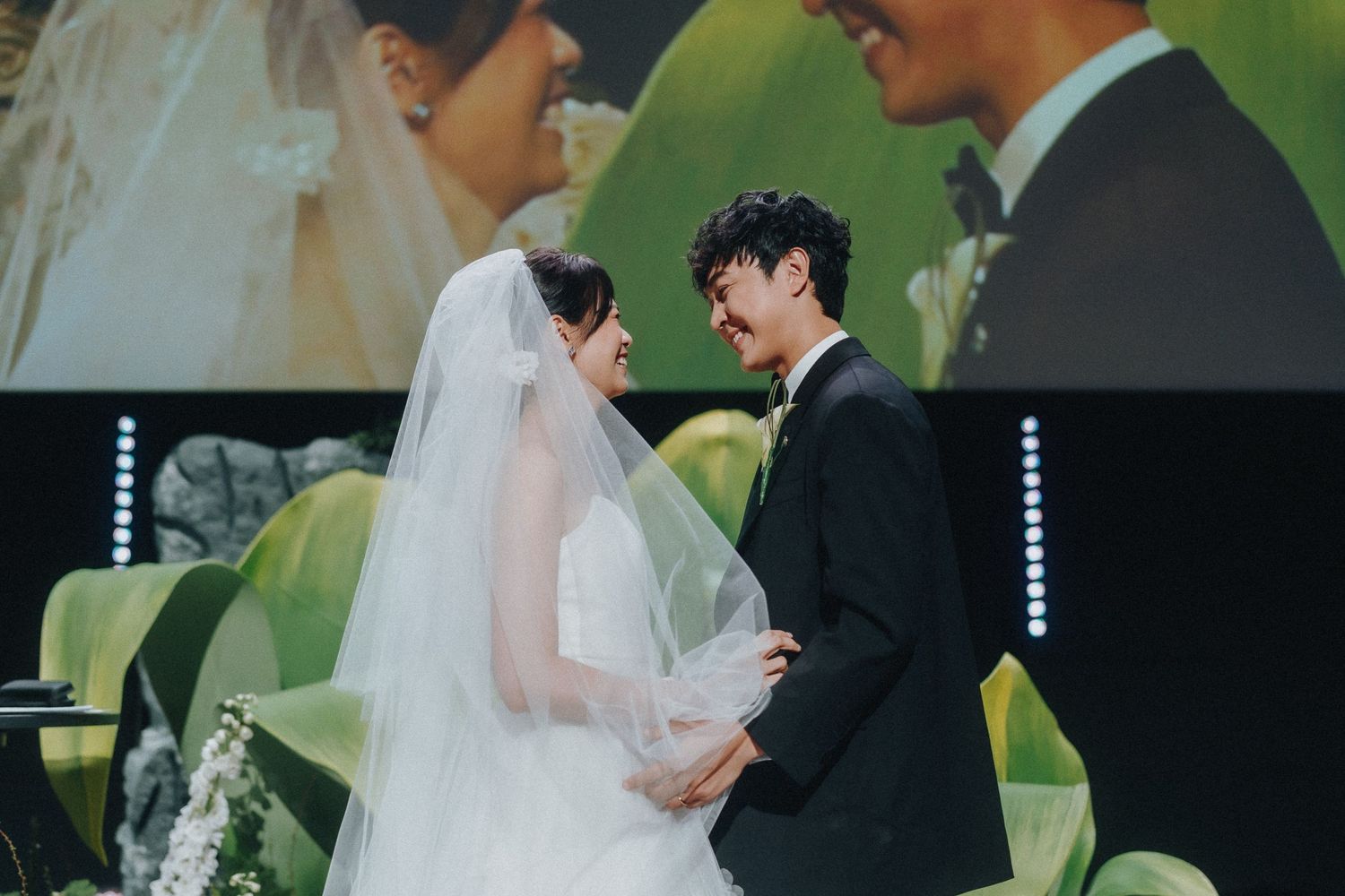 A tender moment between newlyweds during their wedding ceremony with green background.