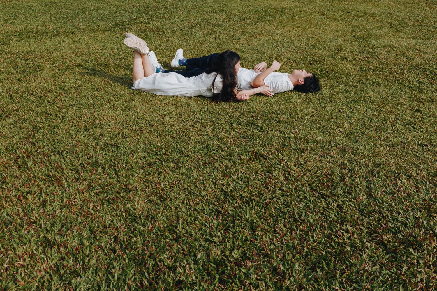 A couple in white clothing lying peacefully on manicured grass from a distance.