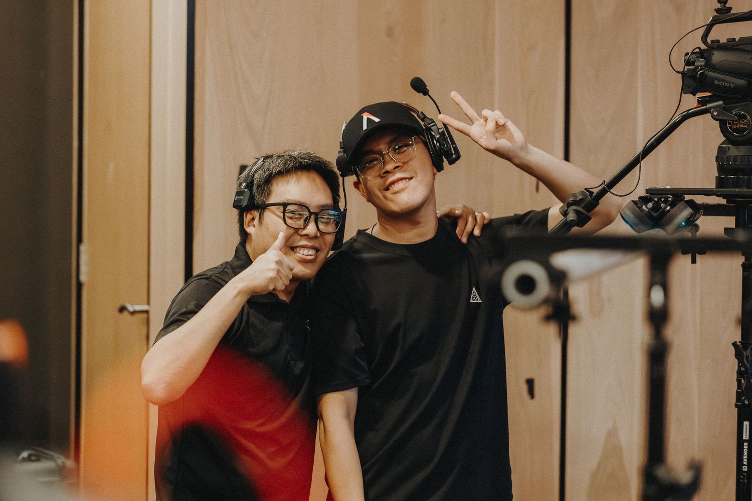 Two people posing together in casual clothing while filming with a camera visible in the shot.
