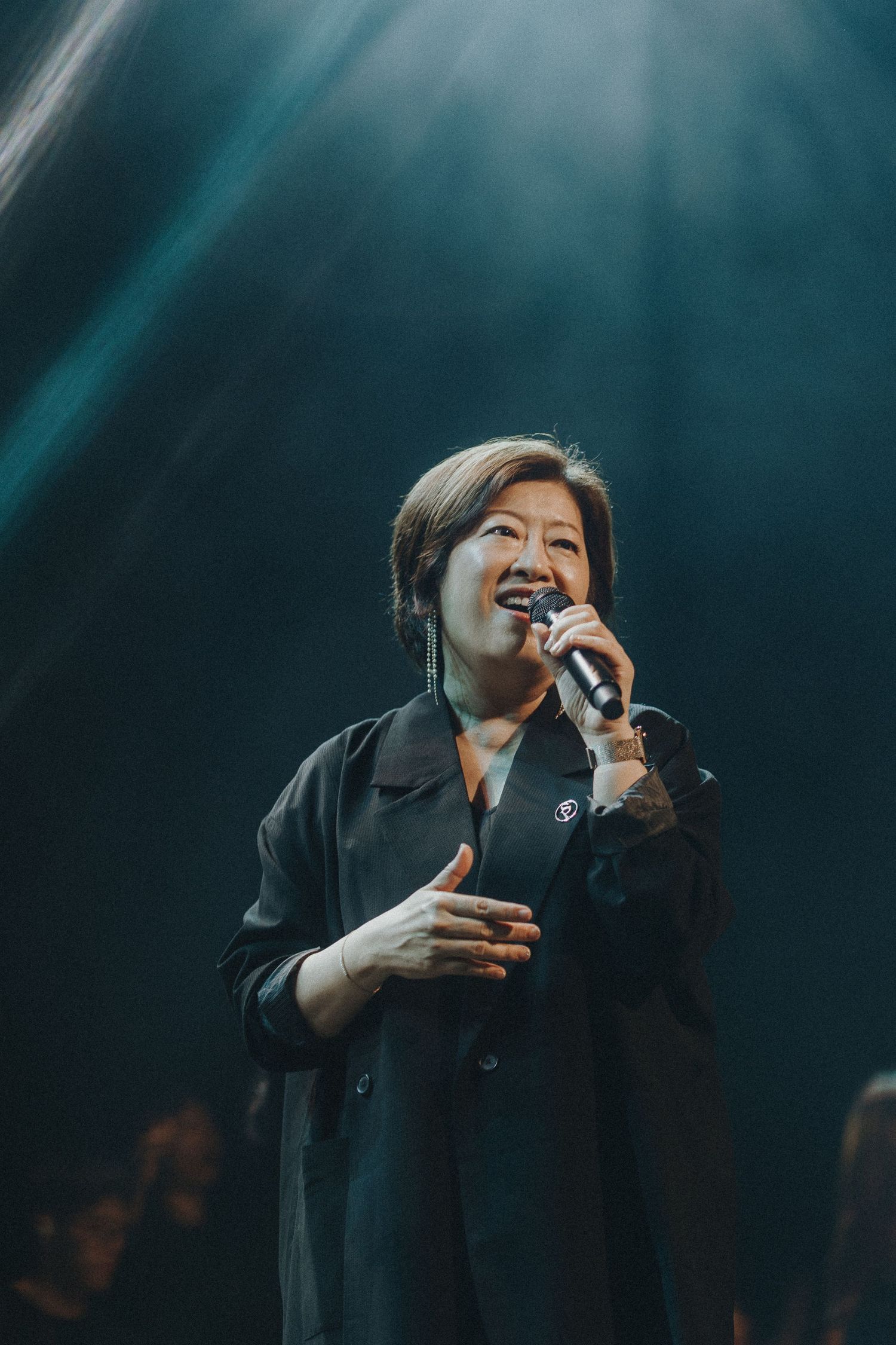 Performer in black attire sings emotionally on stage under dramatic spotlight.