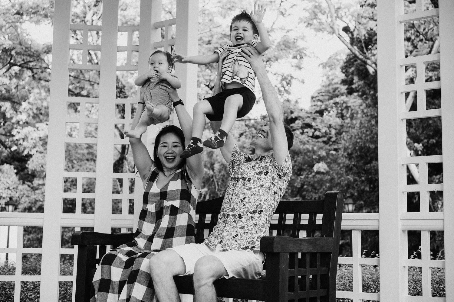 A joyful group plays together on a white lattice garden pergola in black and white photography.