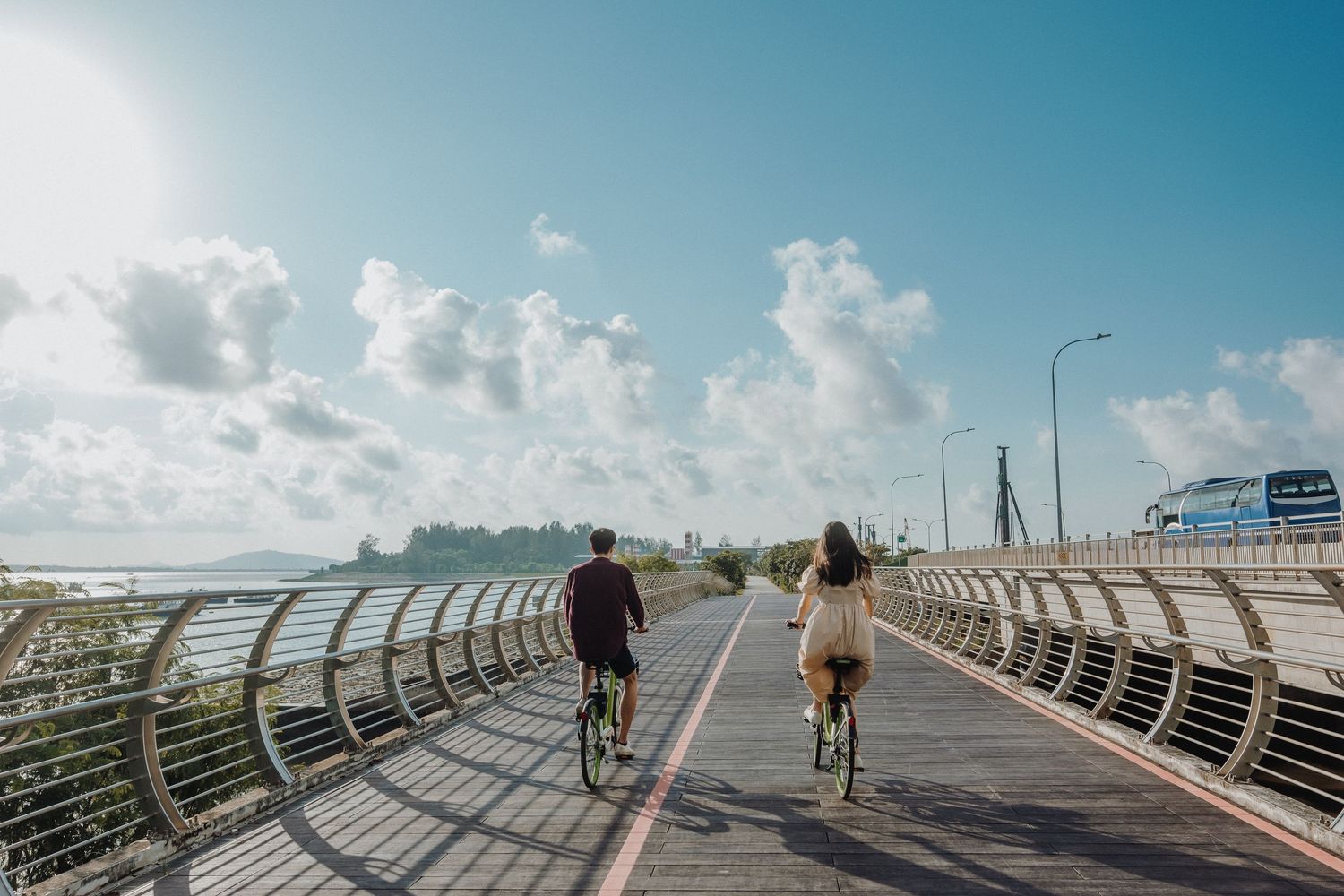 Walking along a curved coastal boardwalk with white metal railings under bright blue sky and puffy clouds.