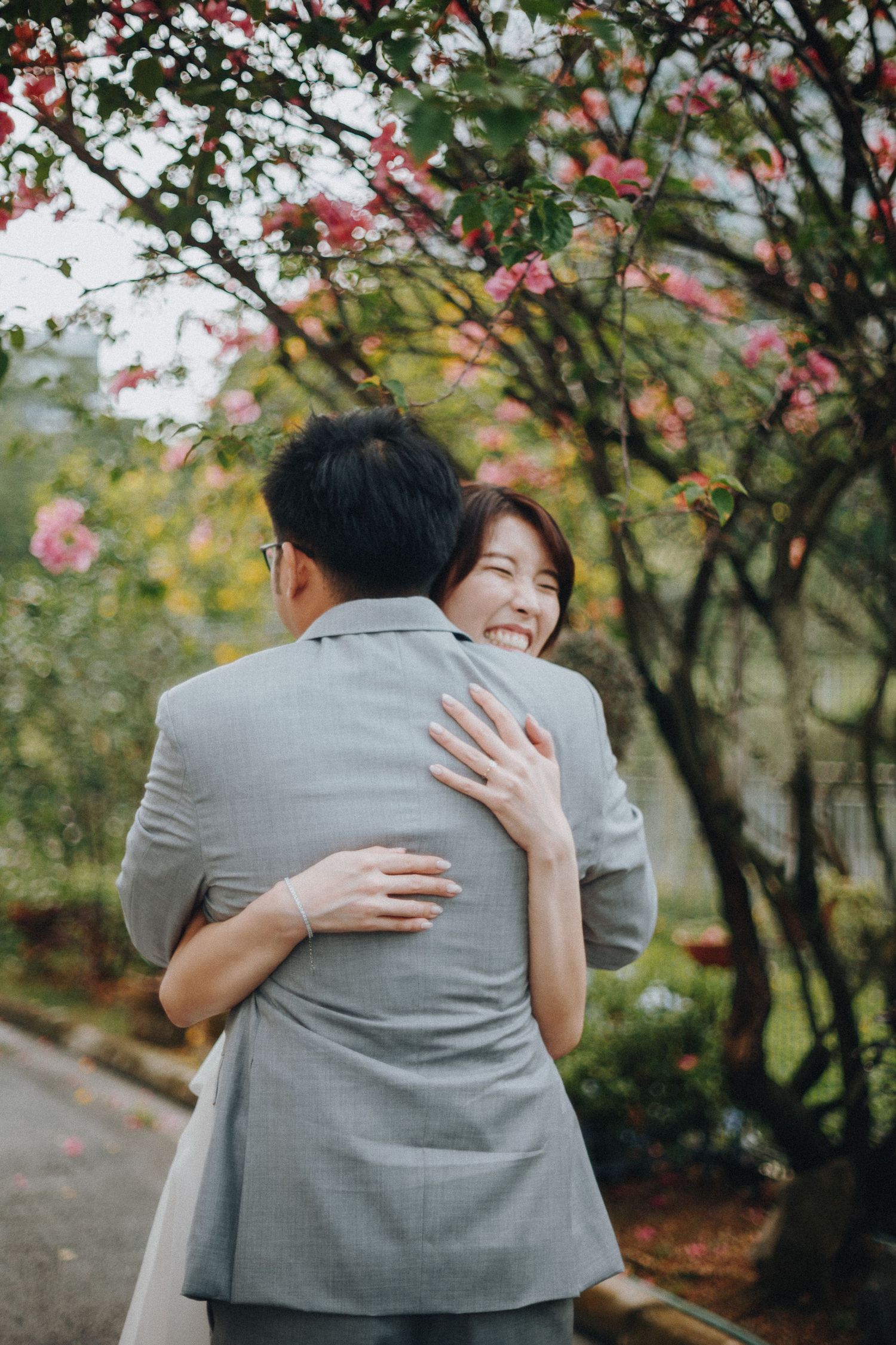 A romantic embrace among blooming cherry blossom trees on a garden path.