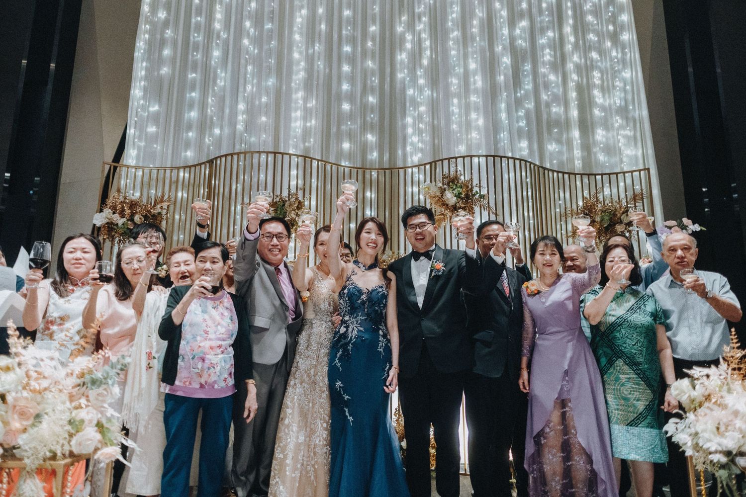 Wedding guests and party members pose against a sparkly curtain backdrop at a reception.