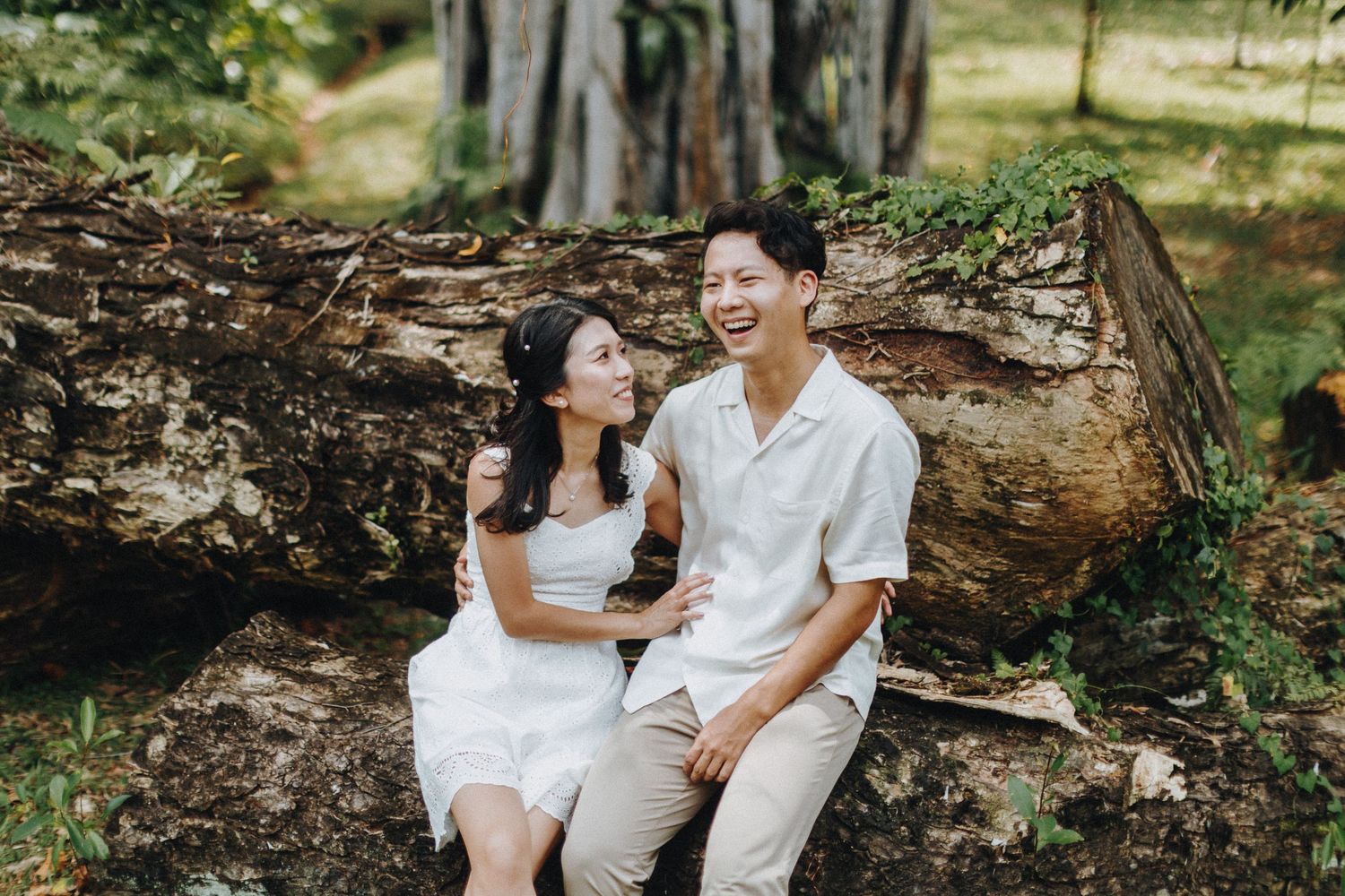 Couple sharing a joyful moment while sitting together against a tree trunk in nature.