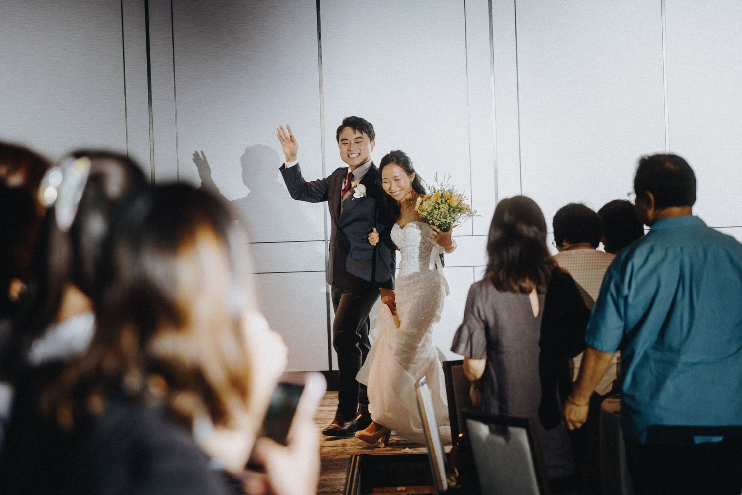 Wedding couple make grand entrance on stage while guests capture the moment.