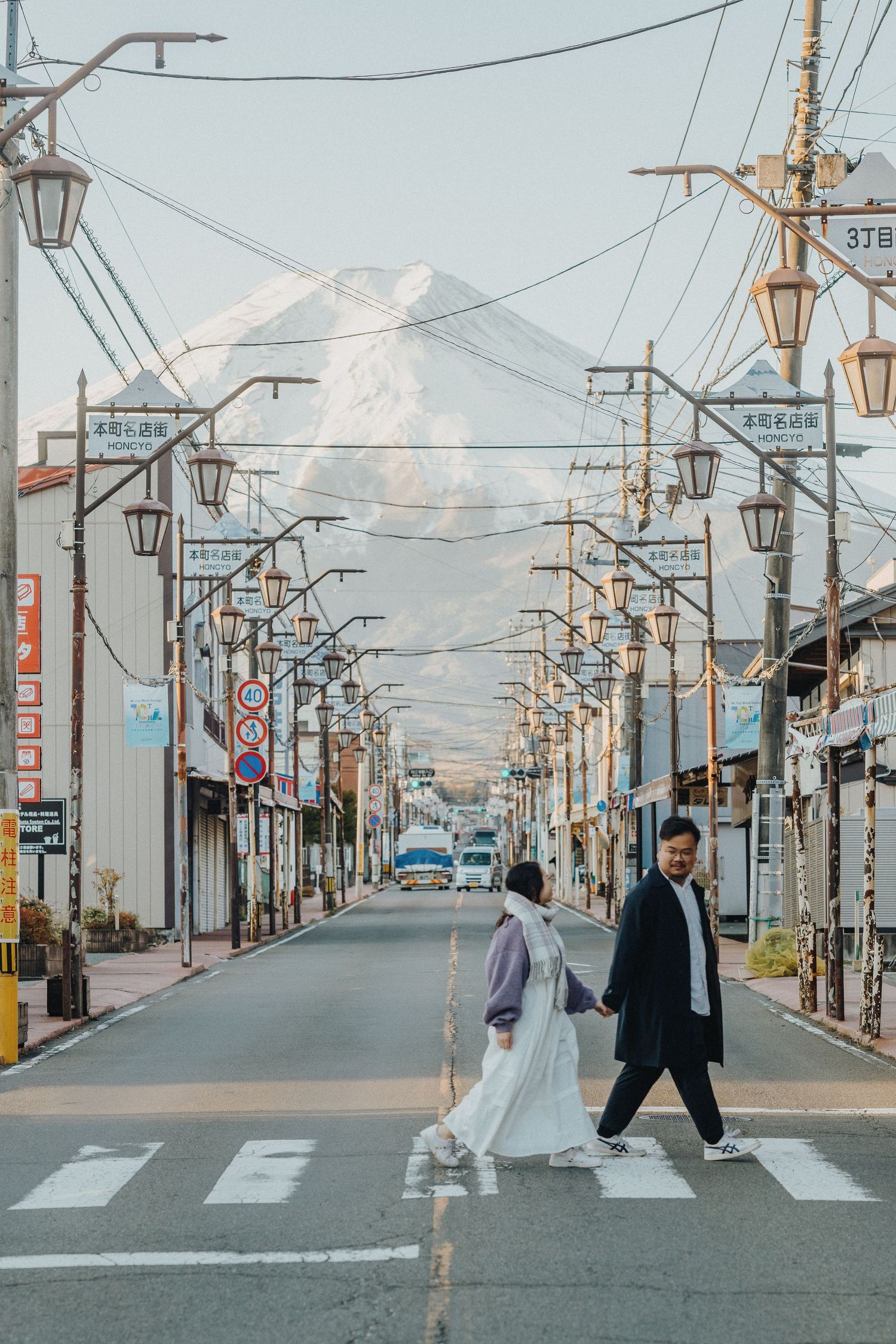 Panoramic view of Mount Fuji visible at the end of a quiet Japanese street with utility poles and traditional lamps.