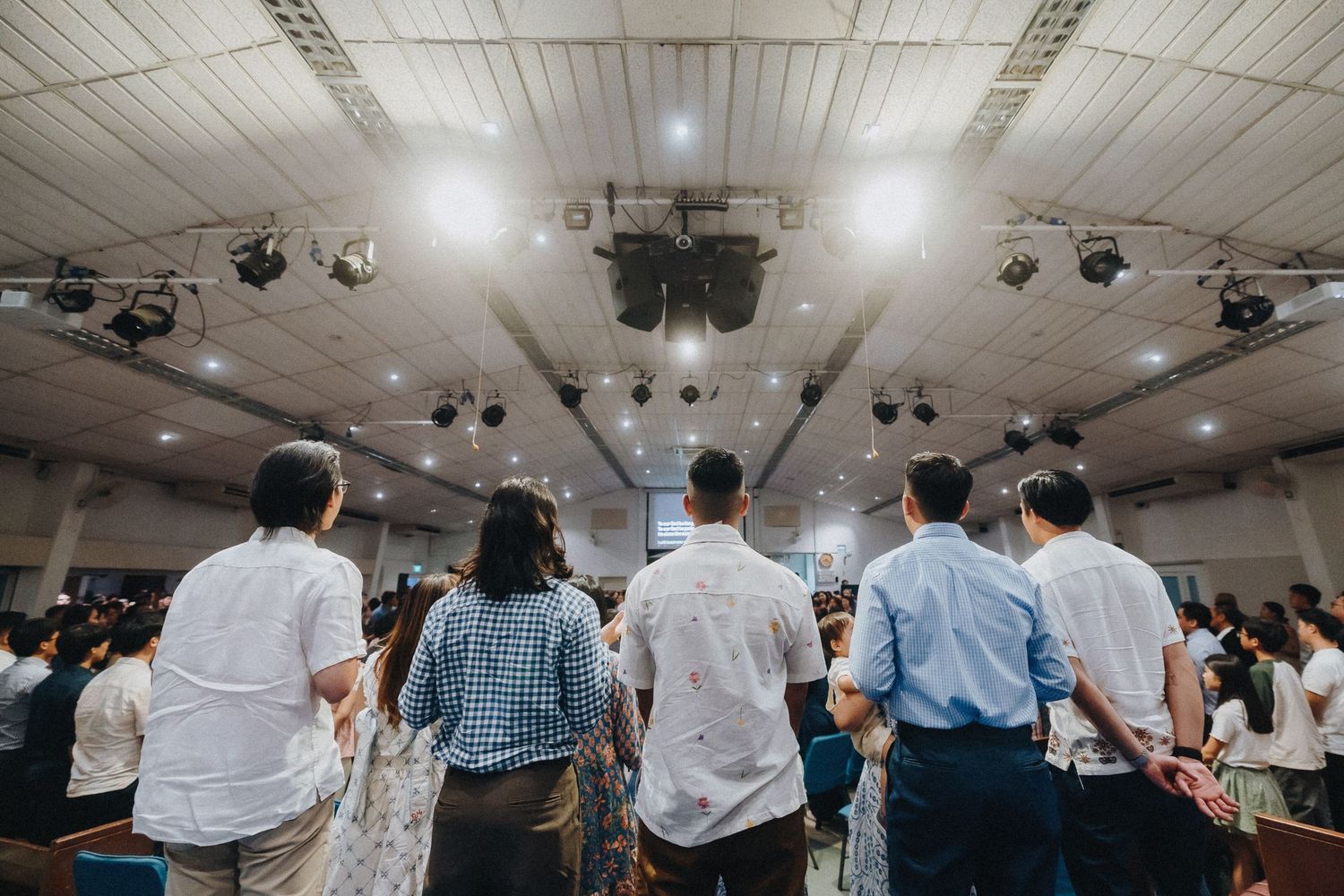 A view from behind of guests standing during a wedding ceremony in a large hall.