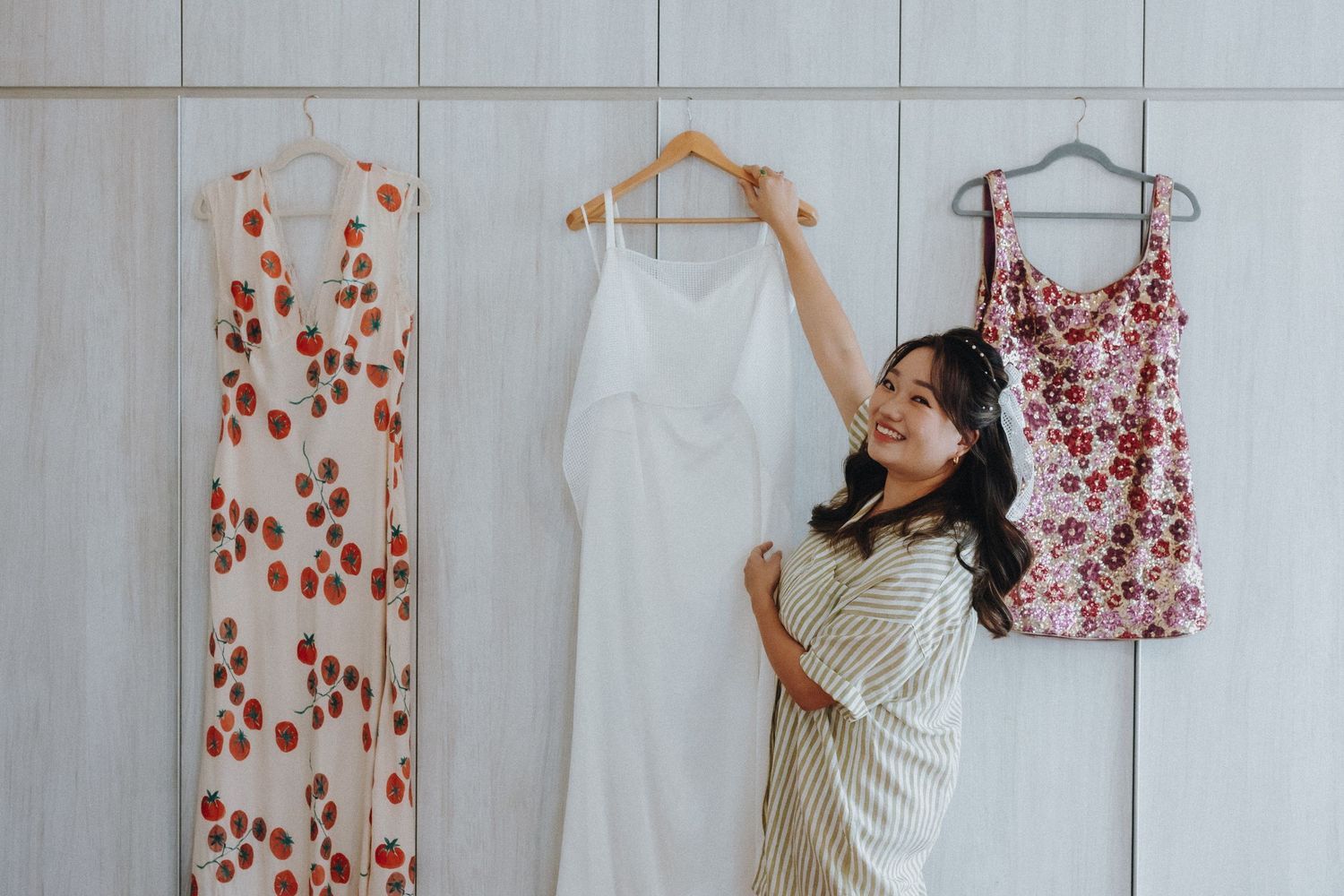 Three floral dresses hanging on display with someone admiring a white garment.