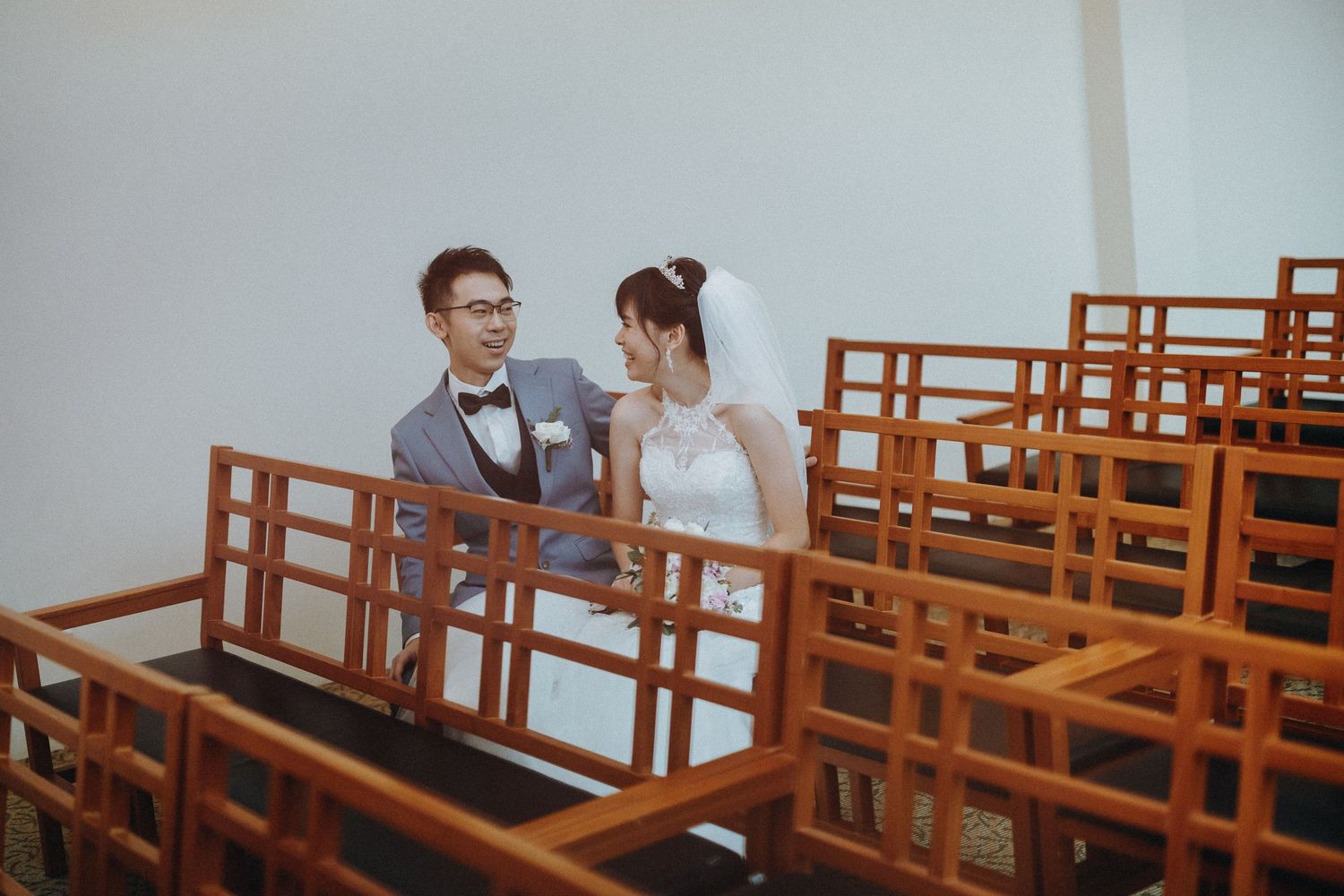 A couple sits intimately together in wooden church pews during what appears to be a quiet moment at their wedding.