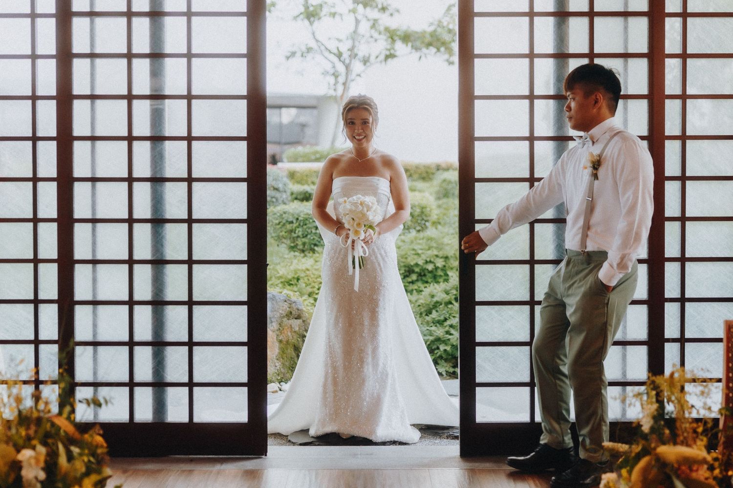 A bride and groom stand in a traditional Japanese venue framed by sliding doors and natural light.