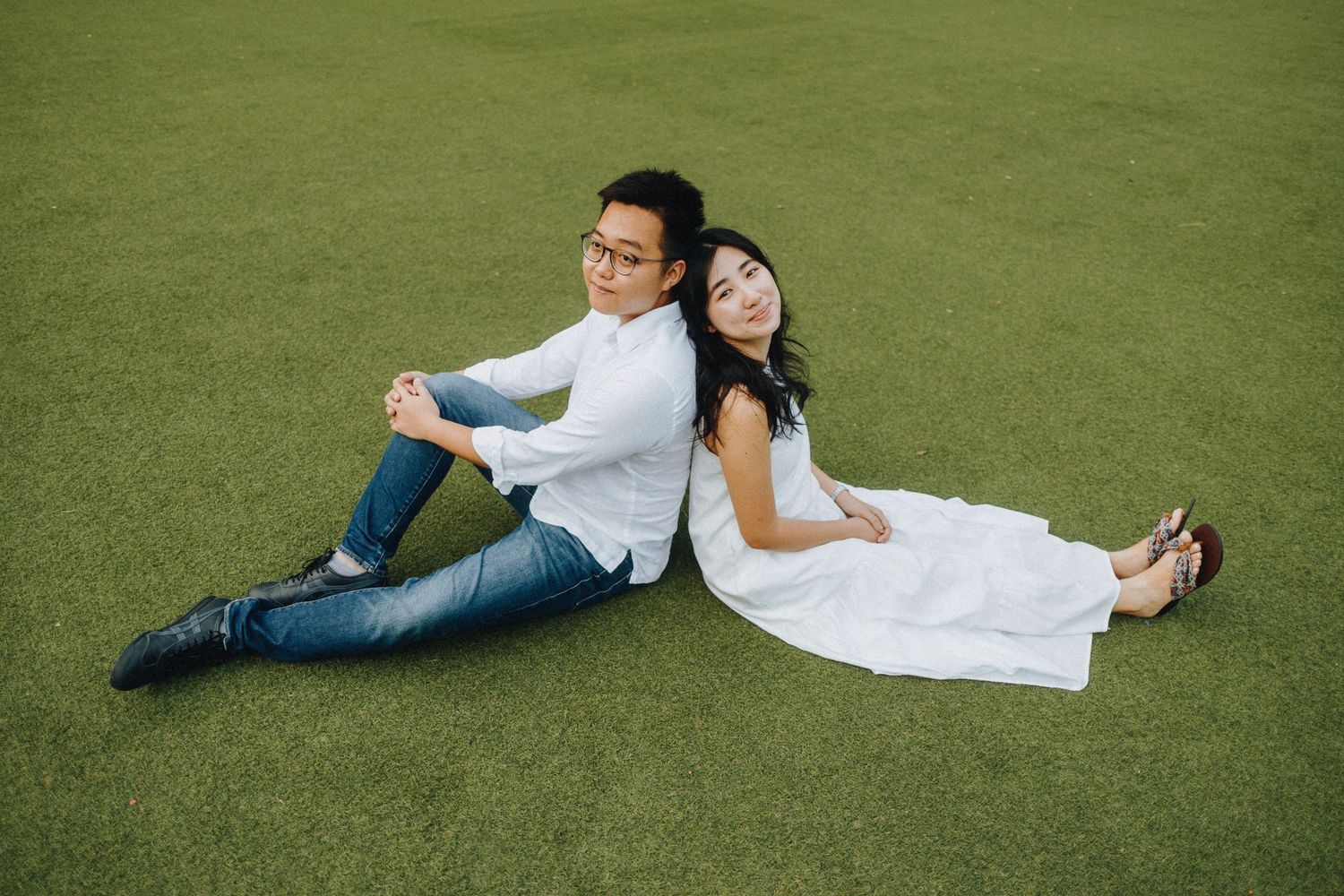 Couple lying on lush green grass enjoying an outdoor photo session at sunset.