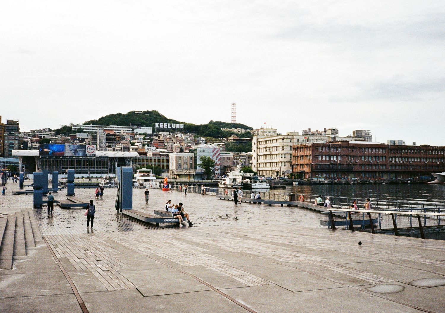 Wide panoramic view of a coastal pier and harbor area on an overcast day.