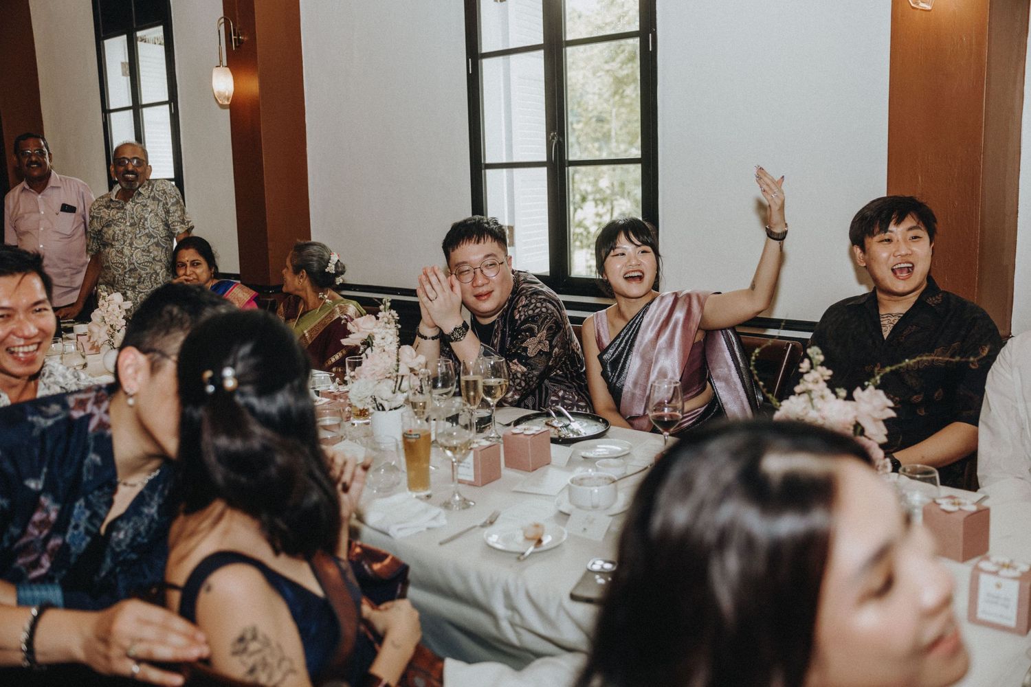 Wedding guests laugh and celebrate joyfully at a decorated reception dinner table.