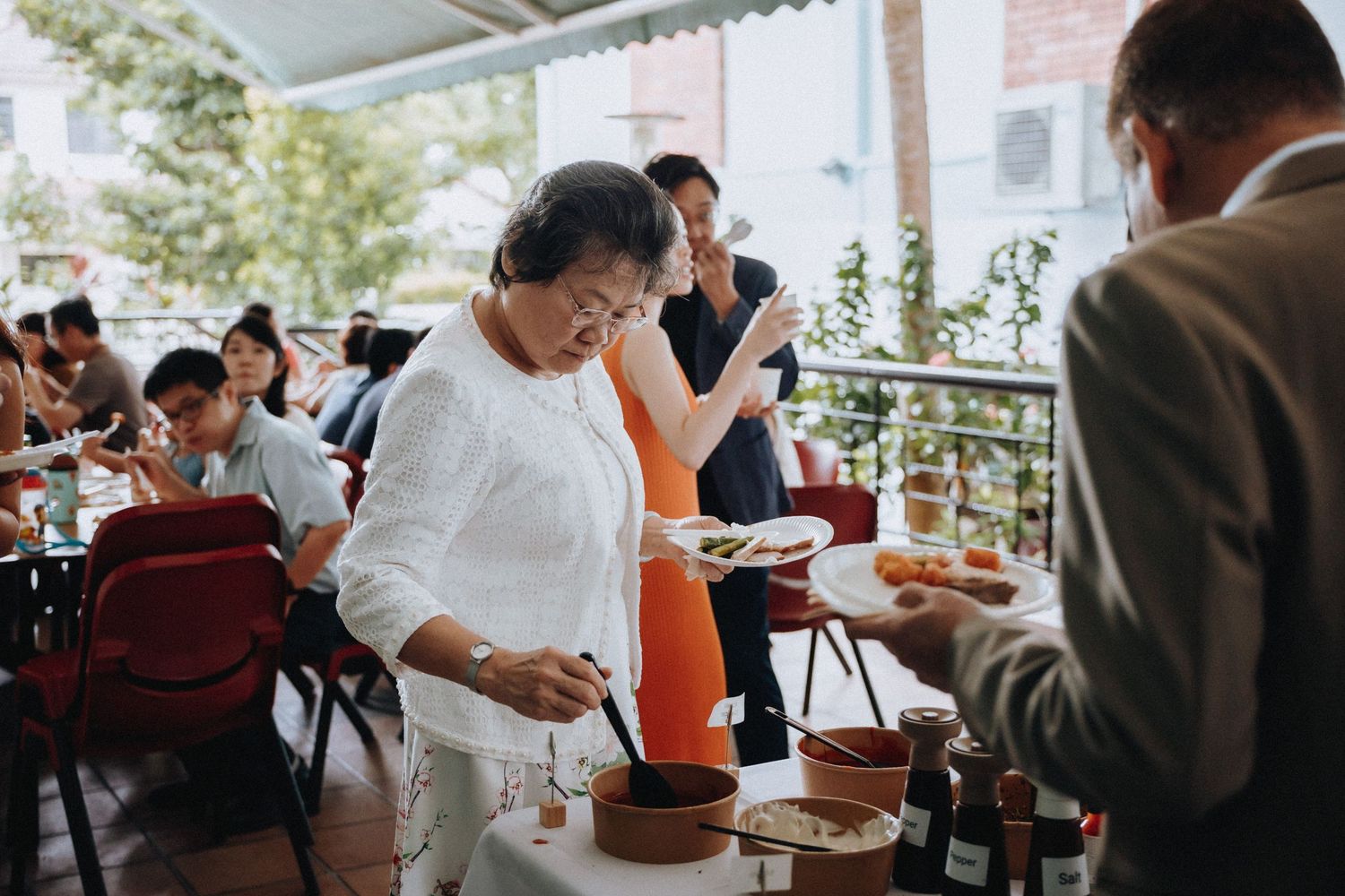 Wedding guests enjoy an outdoor reception buffet on a sunlit terrace with festive food.