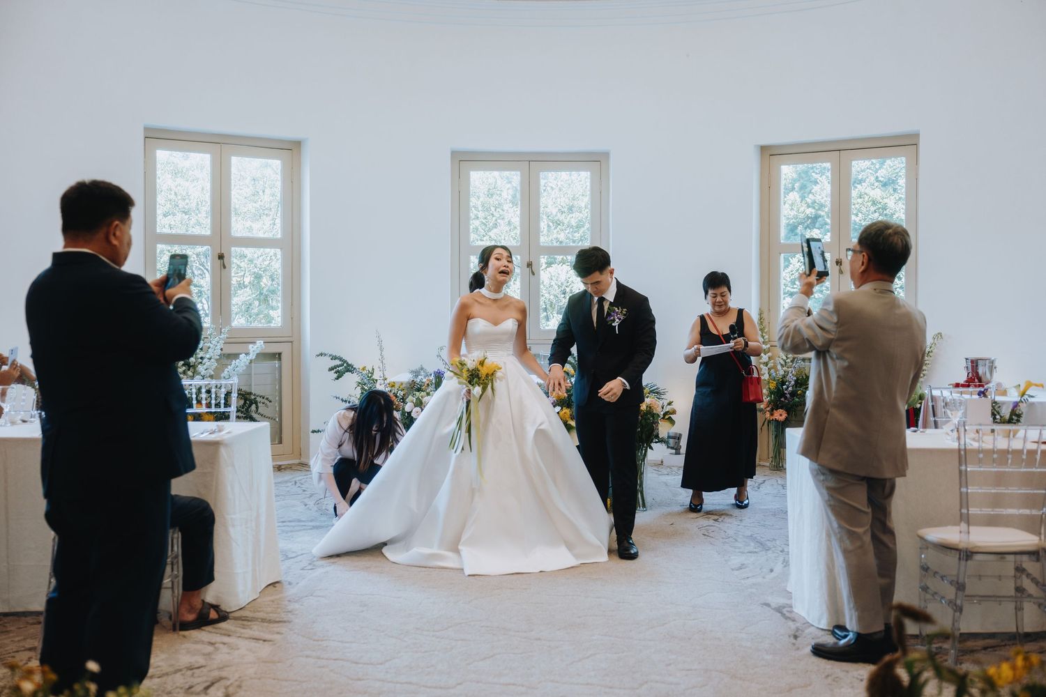 Bride and groom walk hand in hand into elegant white wedding venue surrounded by smiling guests.