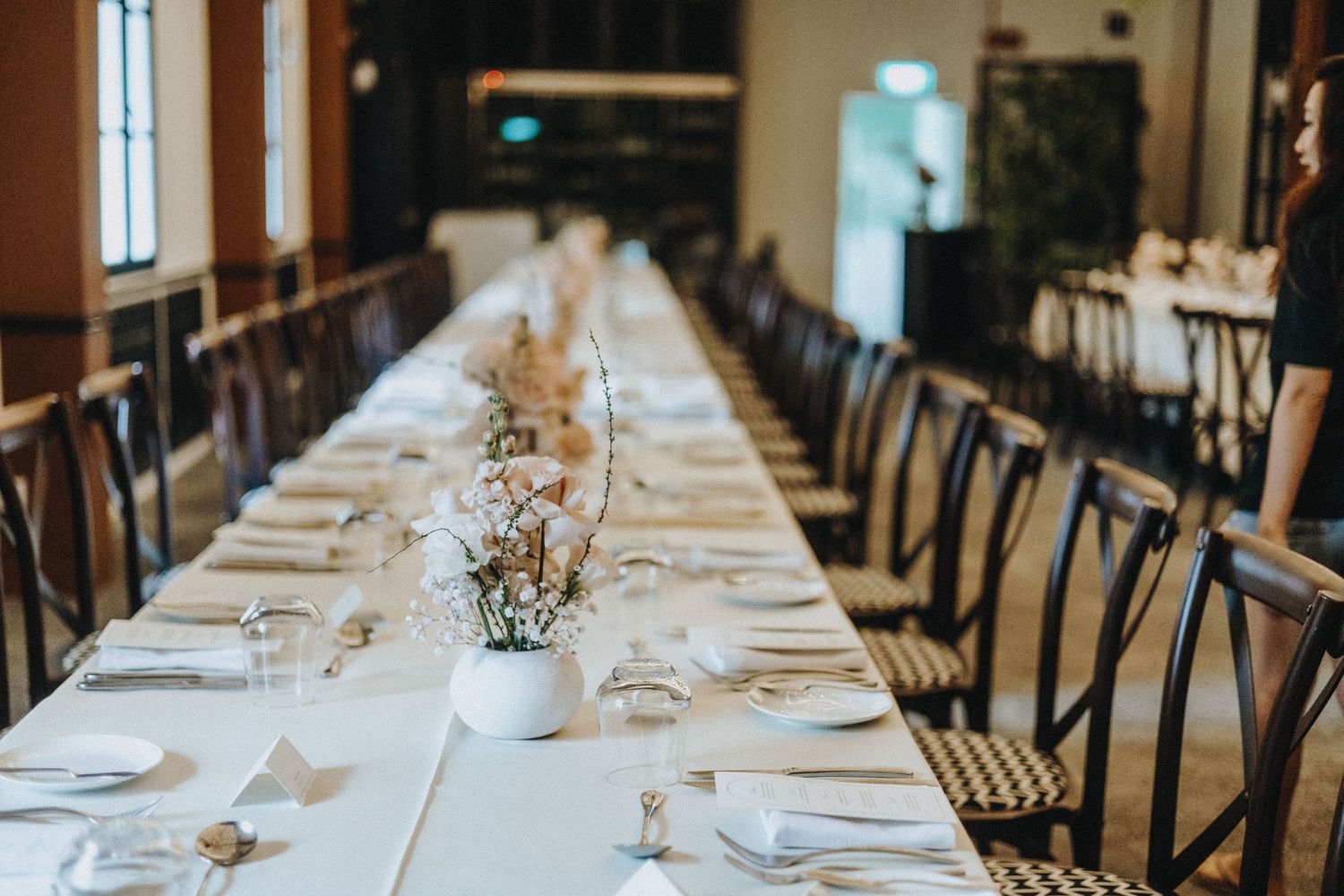 Elegant long wedding reception table set with white linens, floral centerpieces, and fine dinnerware in a warm venue.