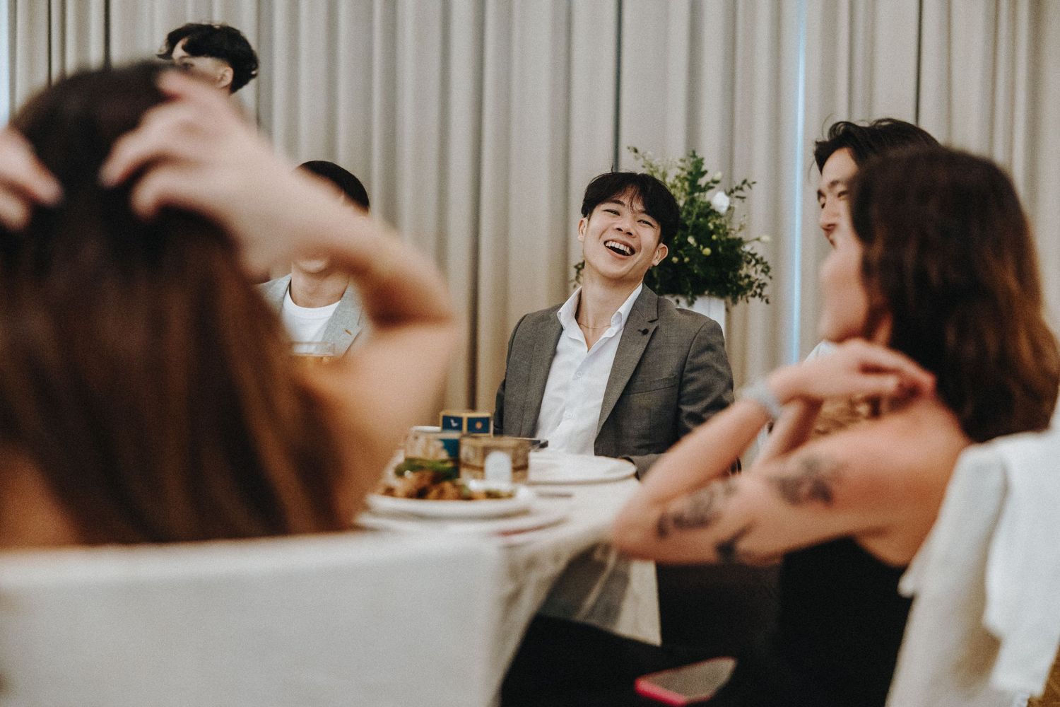 Friends gather around a dining table sharing laughs and conversation during a casual indoor meal together.