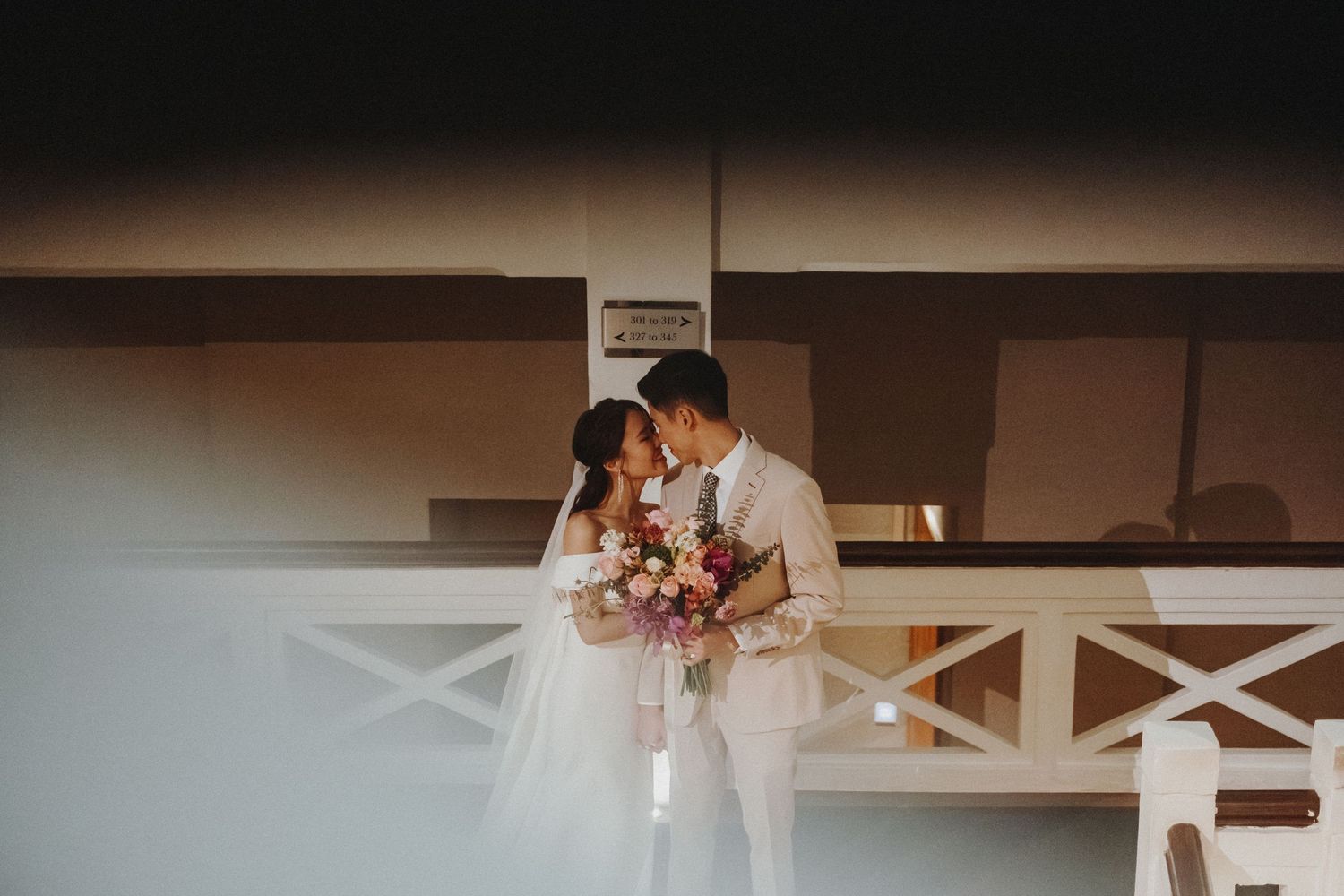 A romantic wedding couple shares an intimate moment with flowers on a balcony at sunset.
