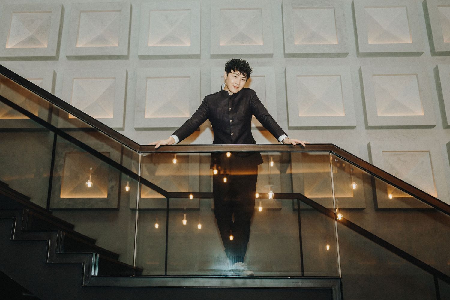 Person in dark outfit descending a modern staircase with geometric white wall panels and hanging pendant lights.