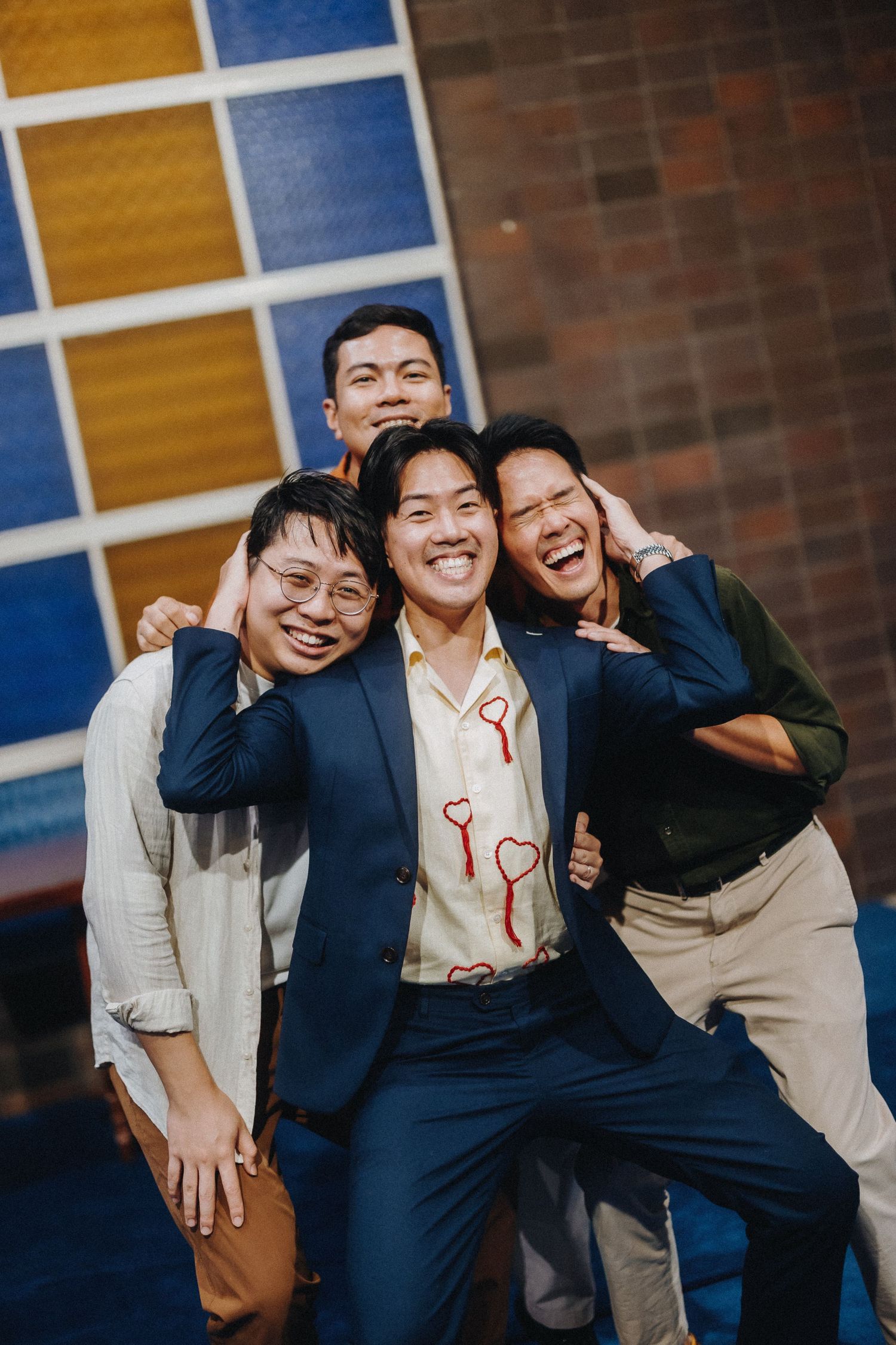 A group poses playfully against a colorful geometric wall background.
