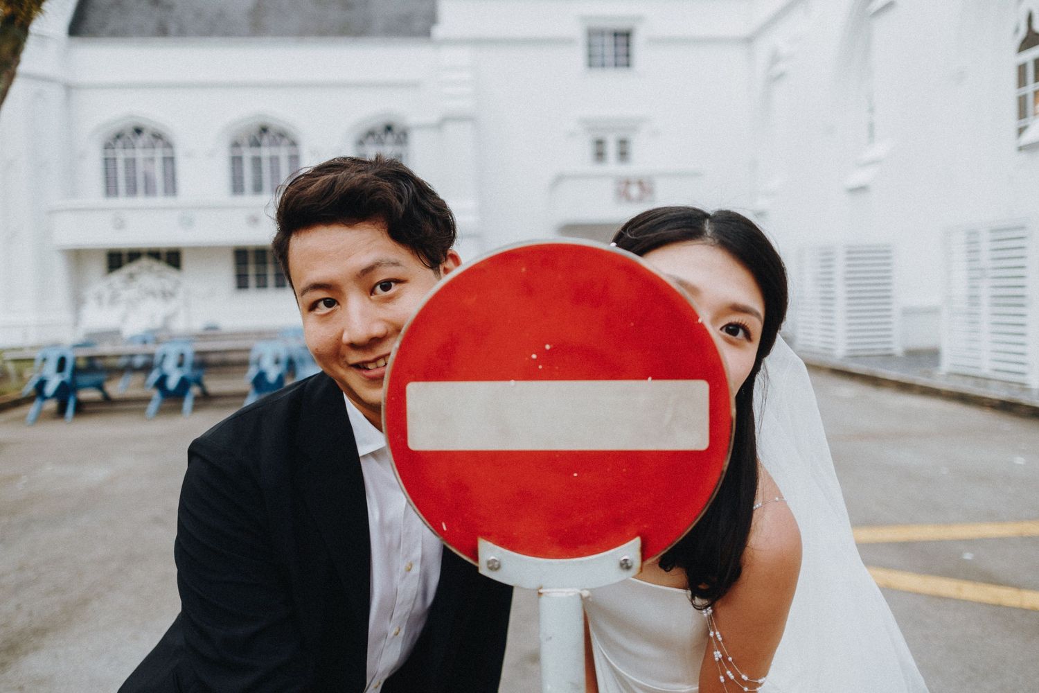 A couple in formal wear poses creatively with a red and white stop sign.