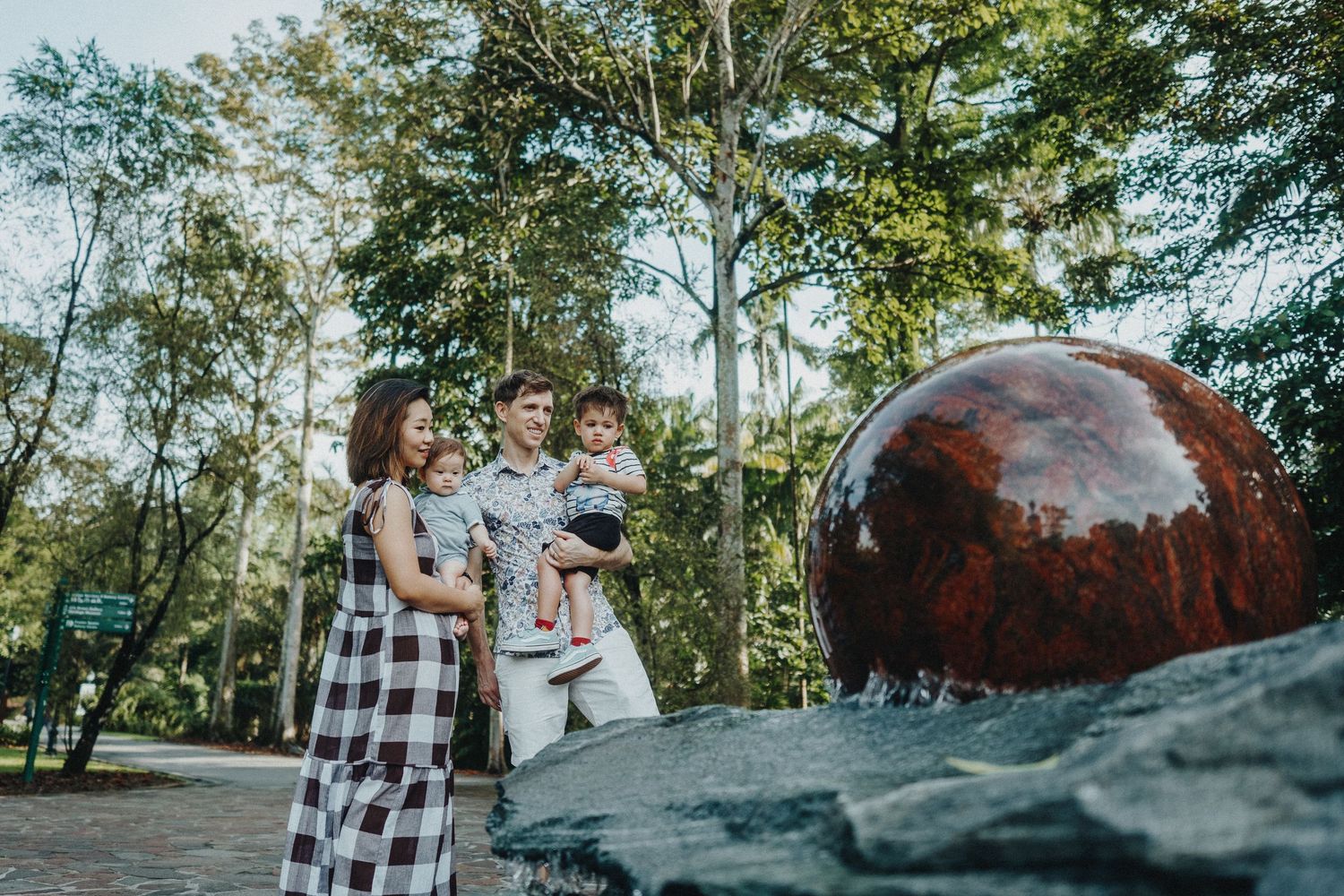 A family poses near a large reflective sphere sculpture in a garden setting.