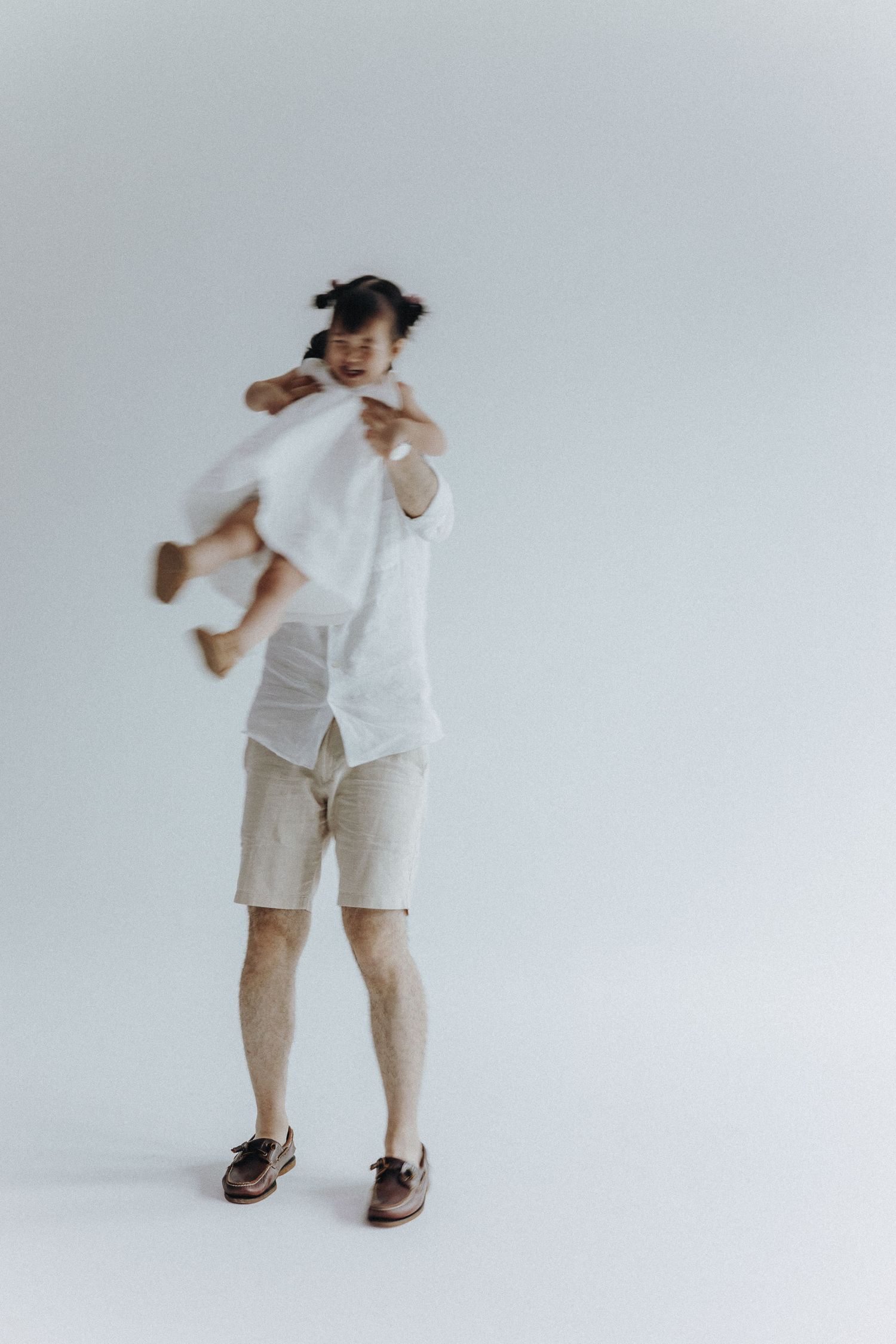 Child in white outfit and pigtails dances playfully against white background.