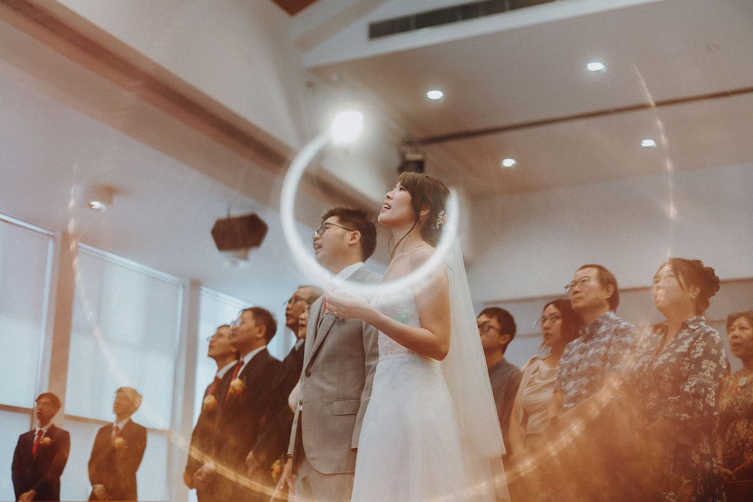 A wedding ceremony in a bright room where guests watch the couple share a celebratory moment.