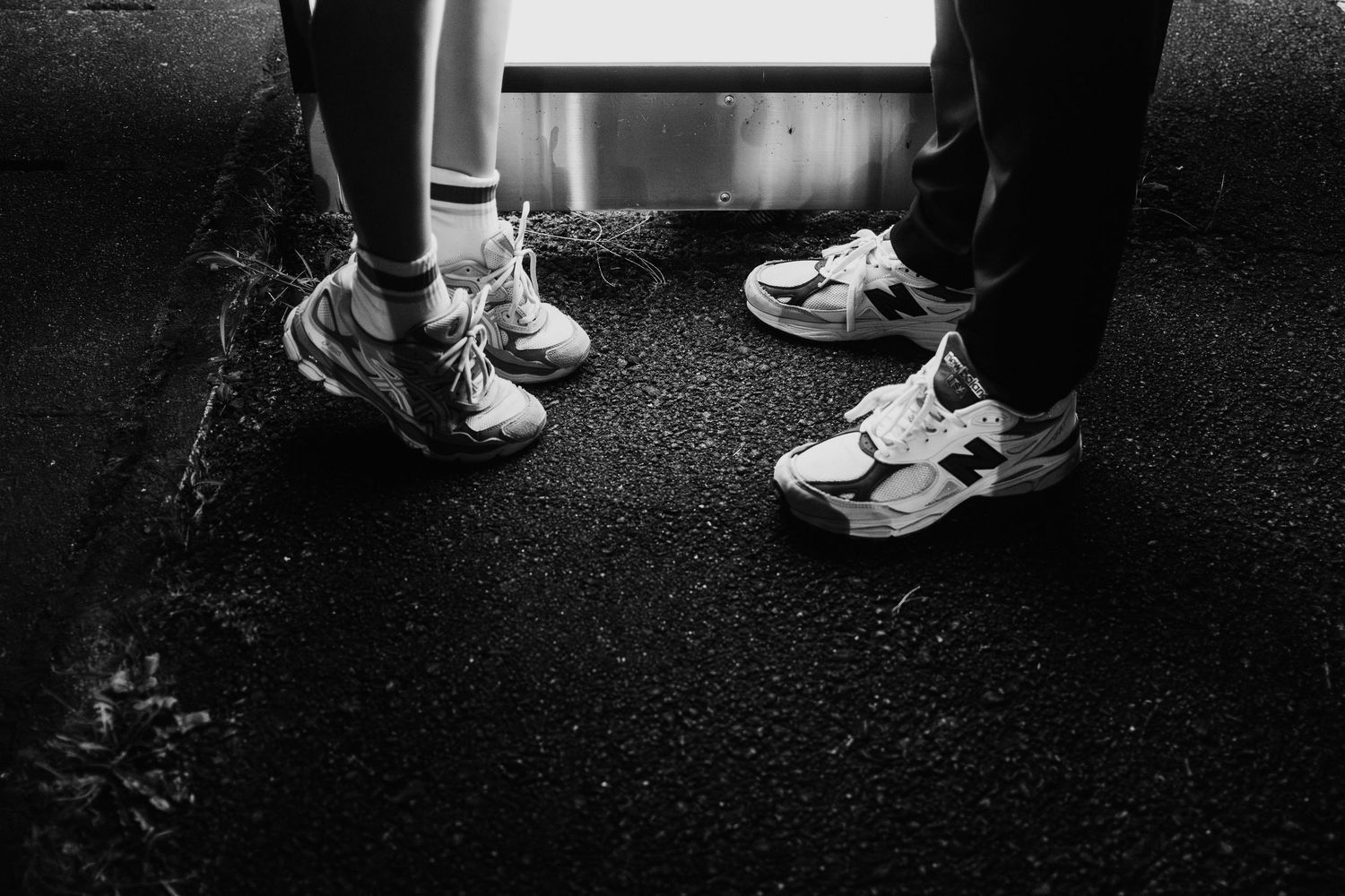 Black and white image showing multiple pairs of feet and shoes on a dark surface.