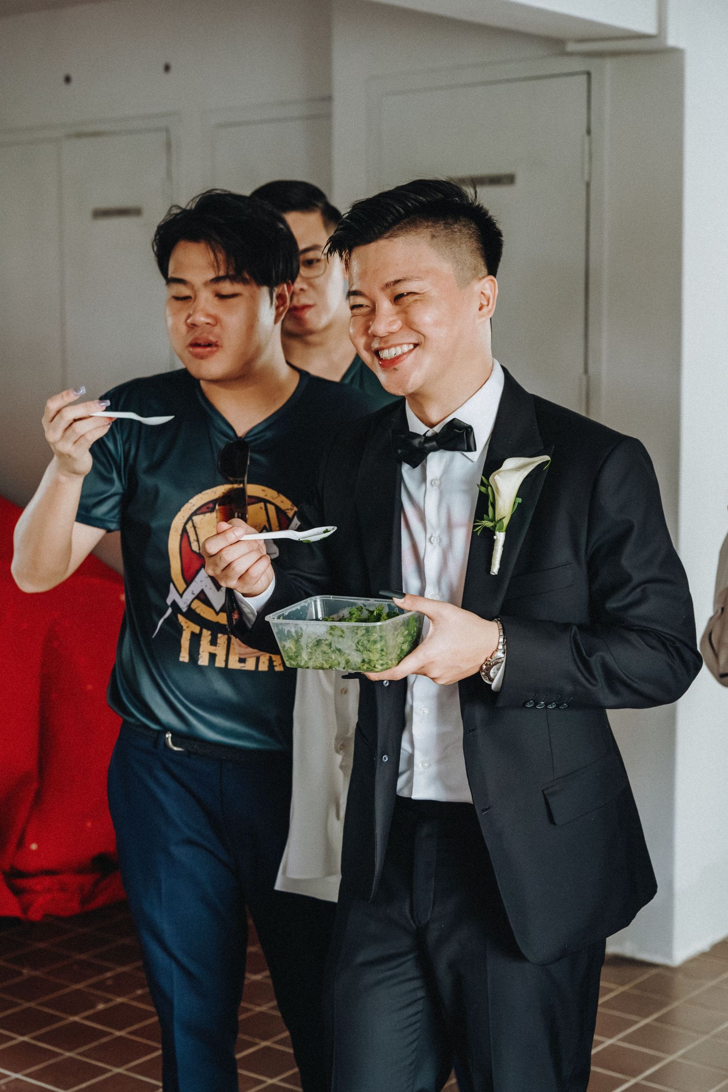 People enjoying food at a casual gathering with one person wearing a formal black tuxedo and boutonniere.