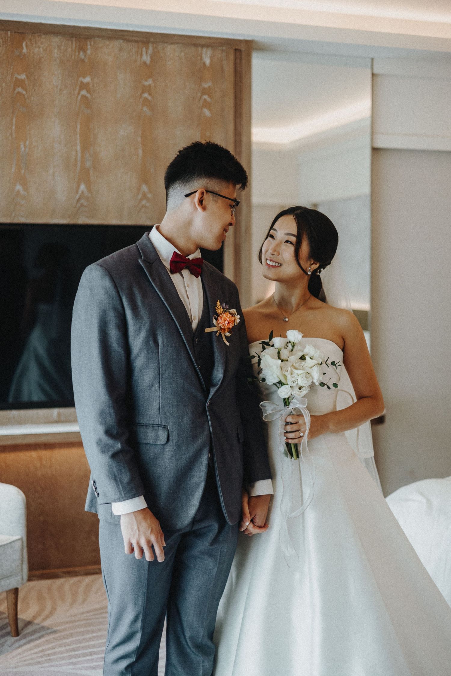 Romantic wedding moment with couple in grey suit and white dress holding a bouquet.