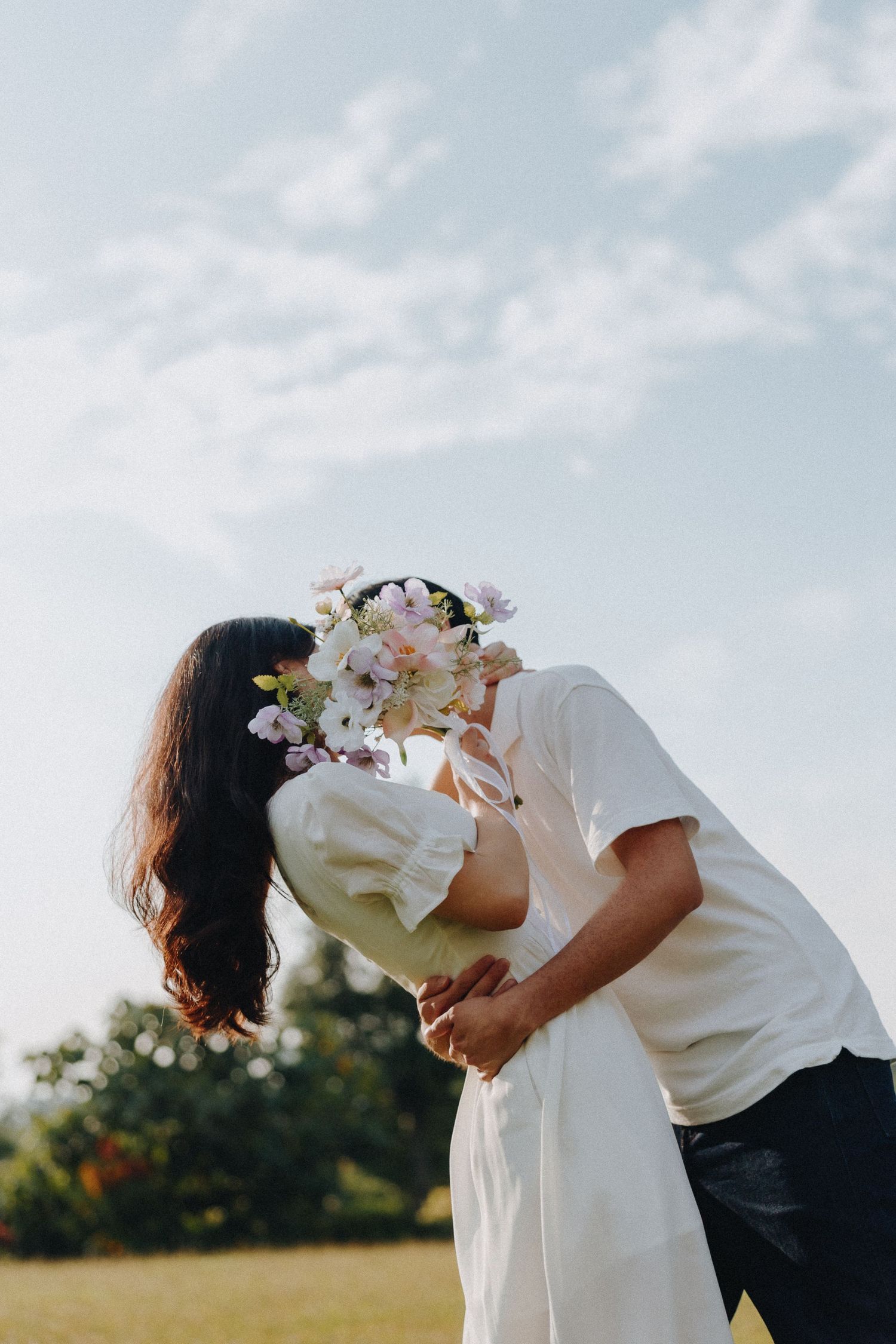 A romantic dip pose with delicate flowers against a bright sky.